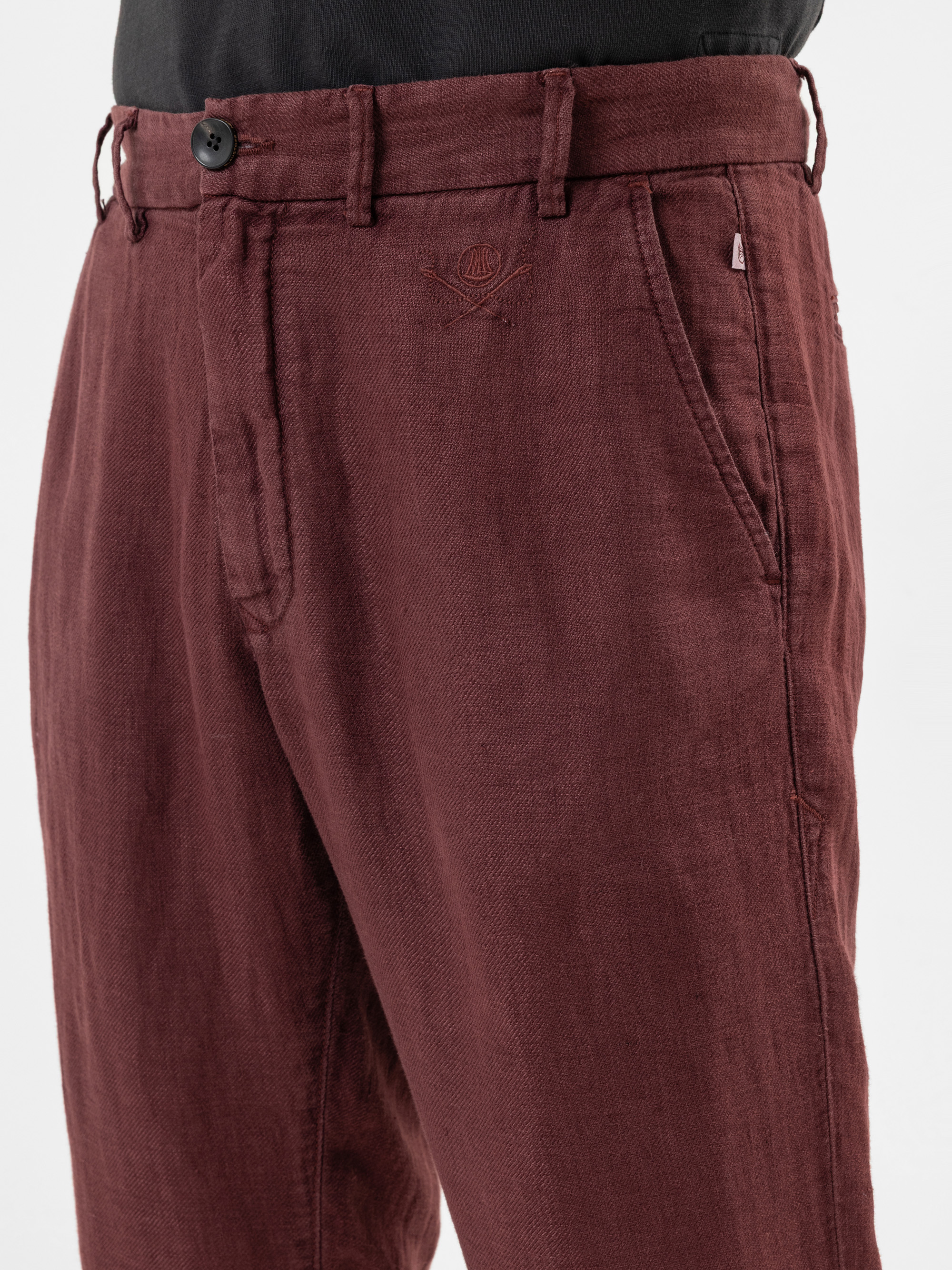 Nahaufnahme einer Person, die eine kastanienbraune Leinenhose mit Seitentaschen und schwarzem Knopfbund trägt, kombiniert mit einem schwarzen Hemd.