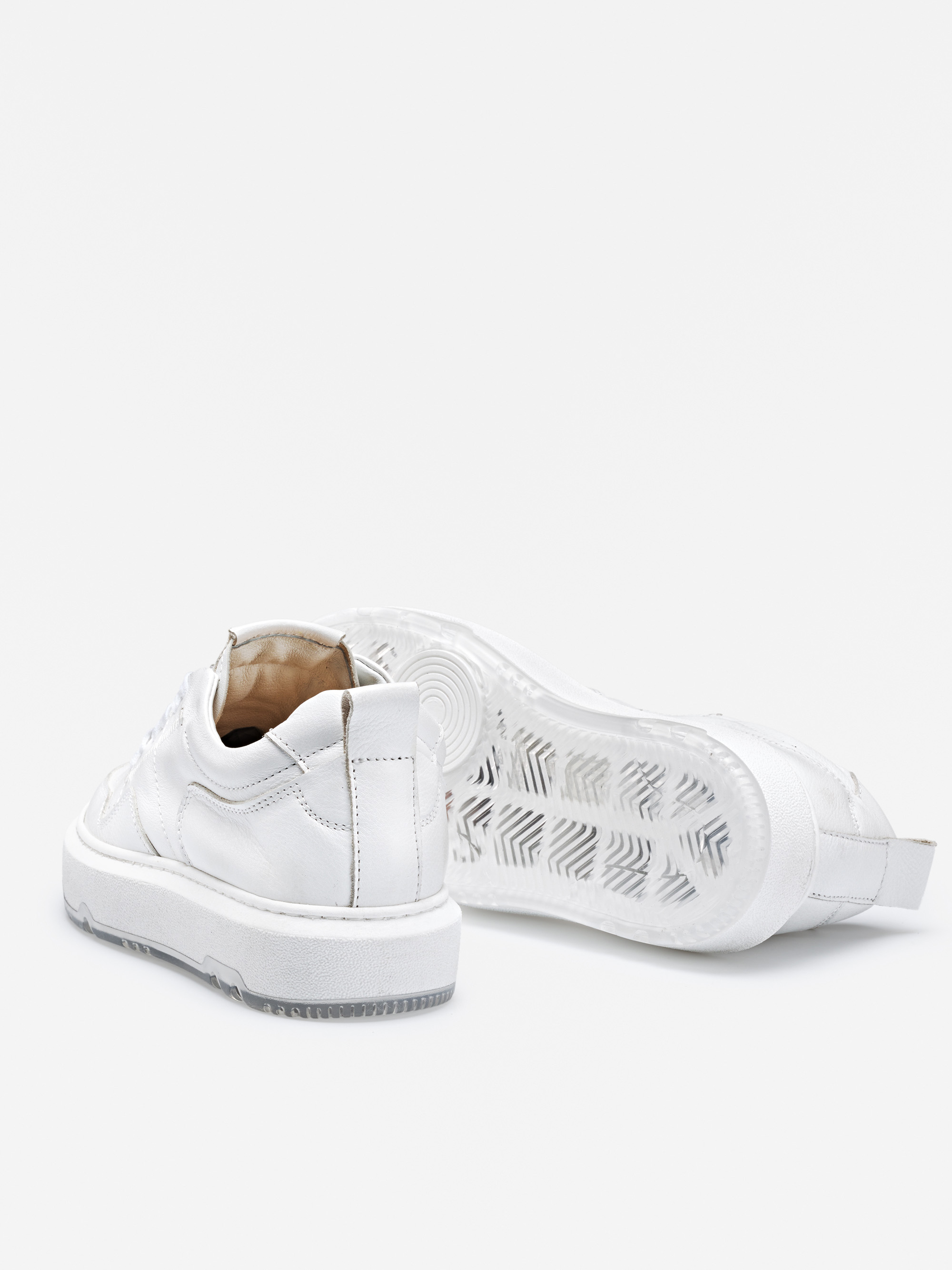 Ein Paar weißer Low-Top-Sneaker auf weißem Hintergrund; ein Schuh steht aufrecht, während der andere auf der Seite liegt und die durchscheinende Gummisohle mit strukturiertem Muster zeigt.