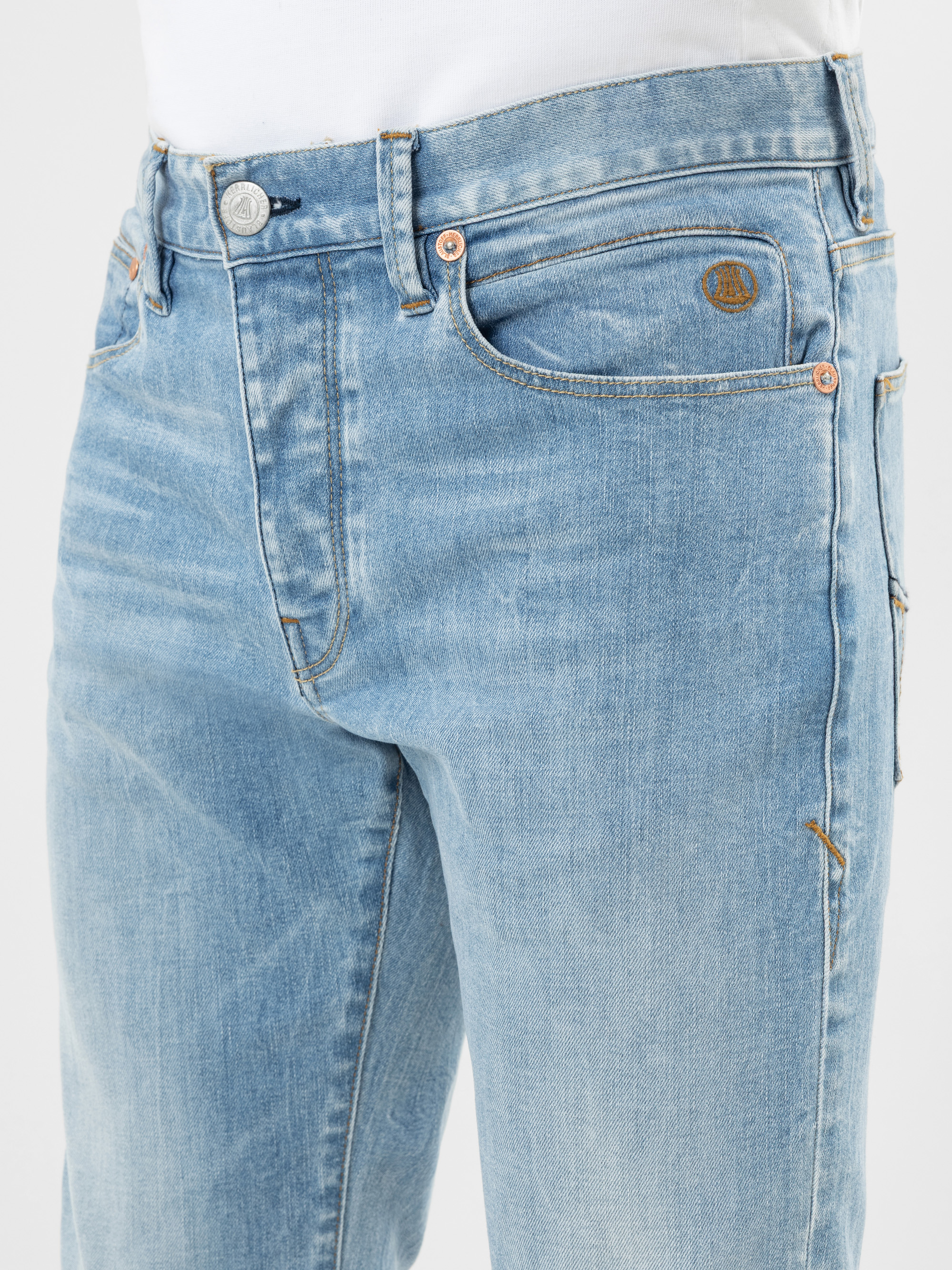 Nahaufnahme einer Person, die eine hellblaue Jeans und ein weißes Hemd trägt, mit Details der Vordertaschen, des Bunds, der Gürtelschlaufen und der verblassten Textur.