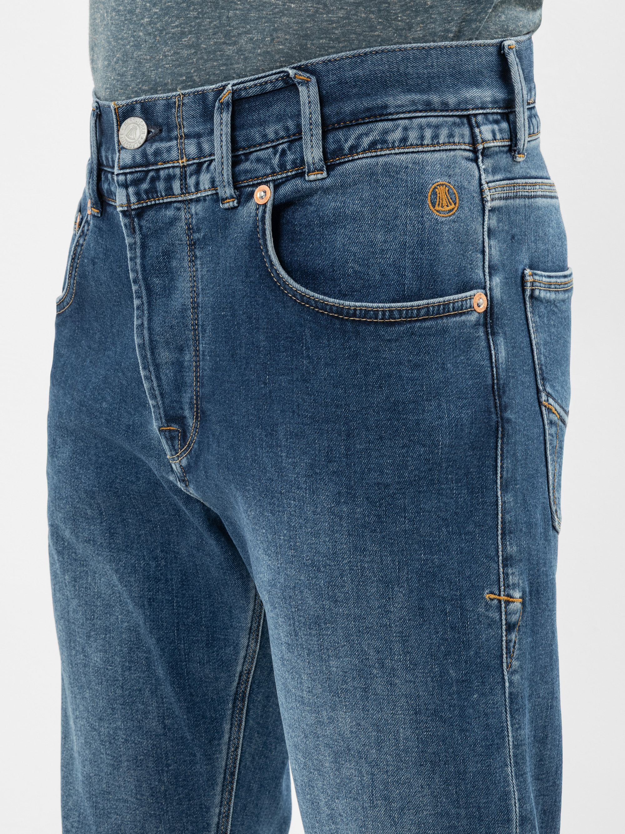 Nahaufnahme einer Person, die eine blaue Jeans und ein graues T-Shirt trägt, wobei die Vordertasche, die Gürtelschlaufen, der Knopf und die Nähte der Jeans zu sehen sind.