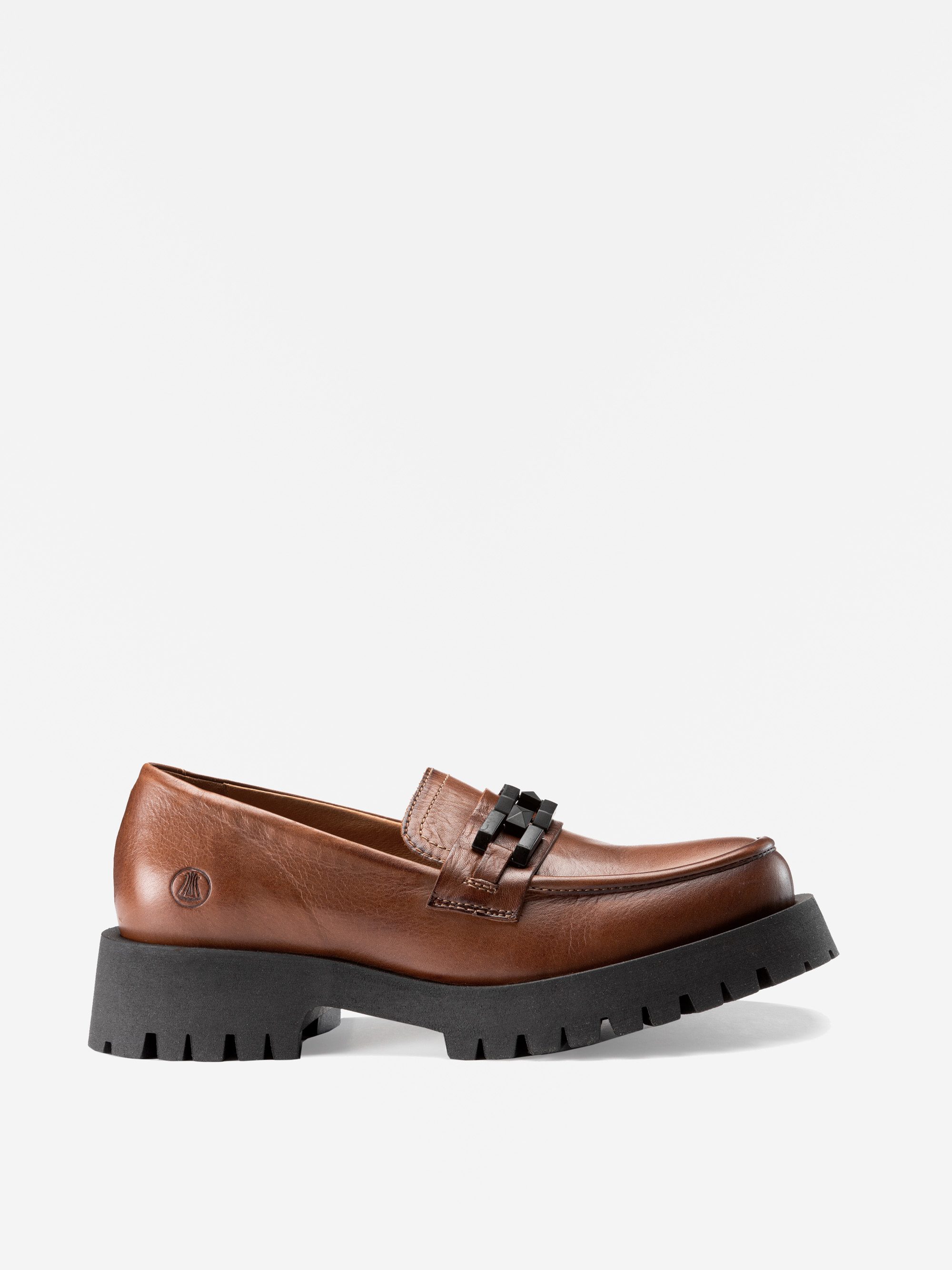 Ein brauner Lederslipper mit einer klobigen schwarzen Gummisohle und einem Absatz, mit einem dekorativen schwarzen Kettendetail auf dem Obermaterial und dezenten Nähten.