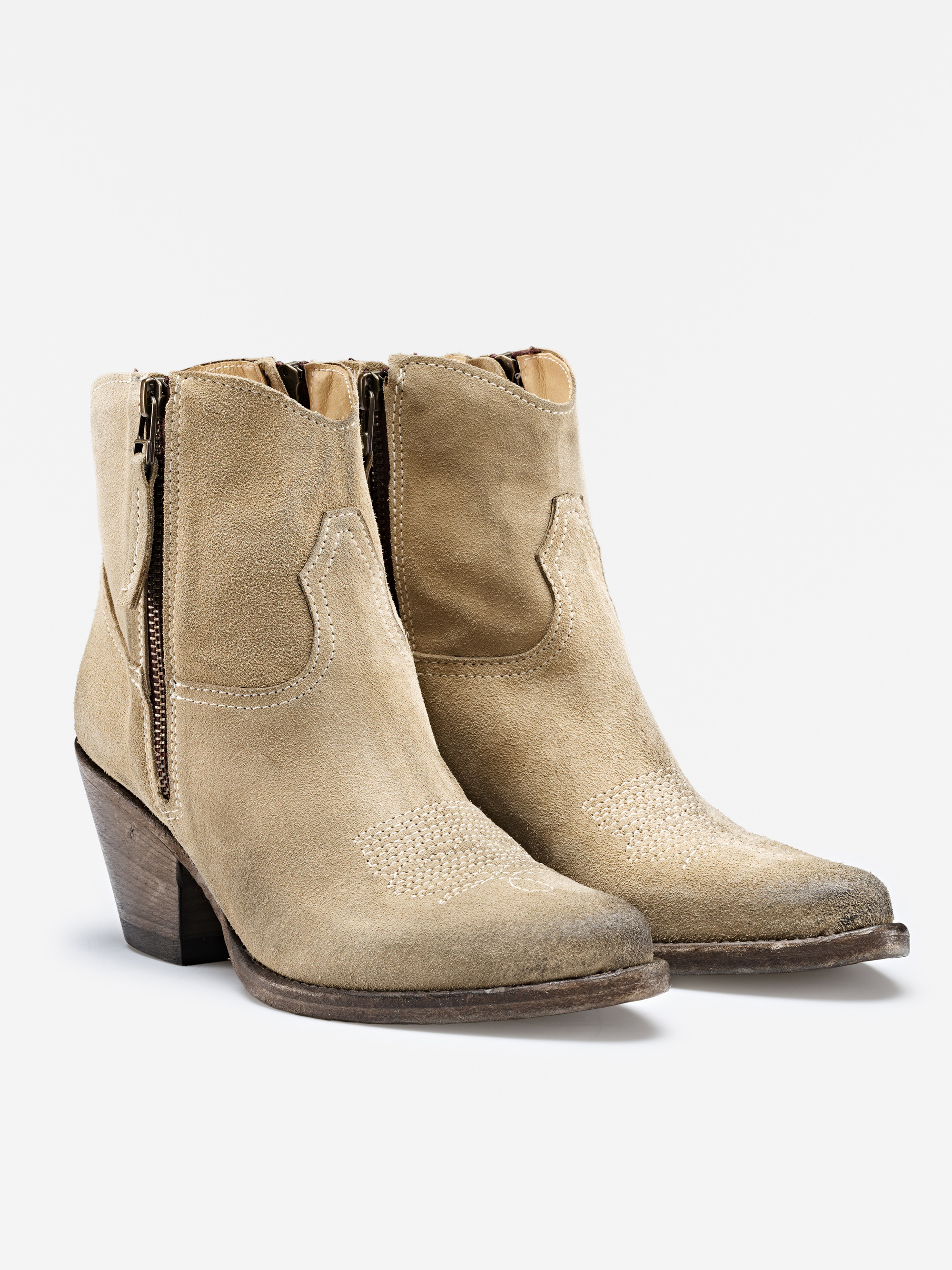 Ein Paar hellbraune Wildlederstiefel mit niedrigem Holzabsatz, seitlichen Reißverschlüssen und Ziernähten an den Zehen, fotografiert auf weißem Hintergrund.