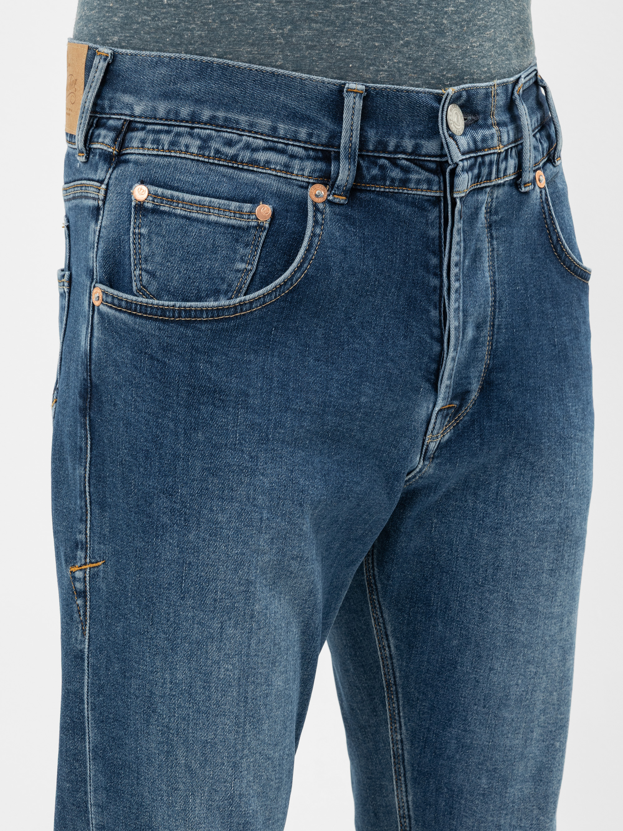 Nahaufnahme einer Person, die Blue Denim Jeans und ein graues Hemd trägt. Die Jeans hat kupferne Nieten, Vordertaschen und sichtbare Nähte. Nur der untere Teil des Oberkörpers und die Oberschenkel sind zu sehen.