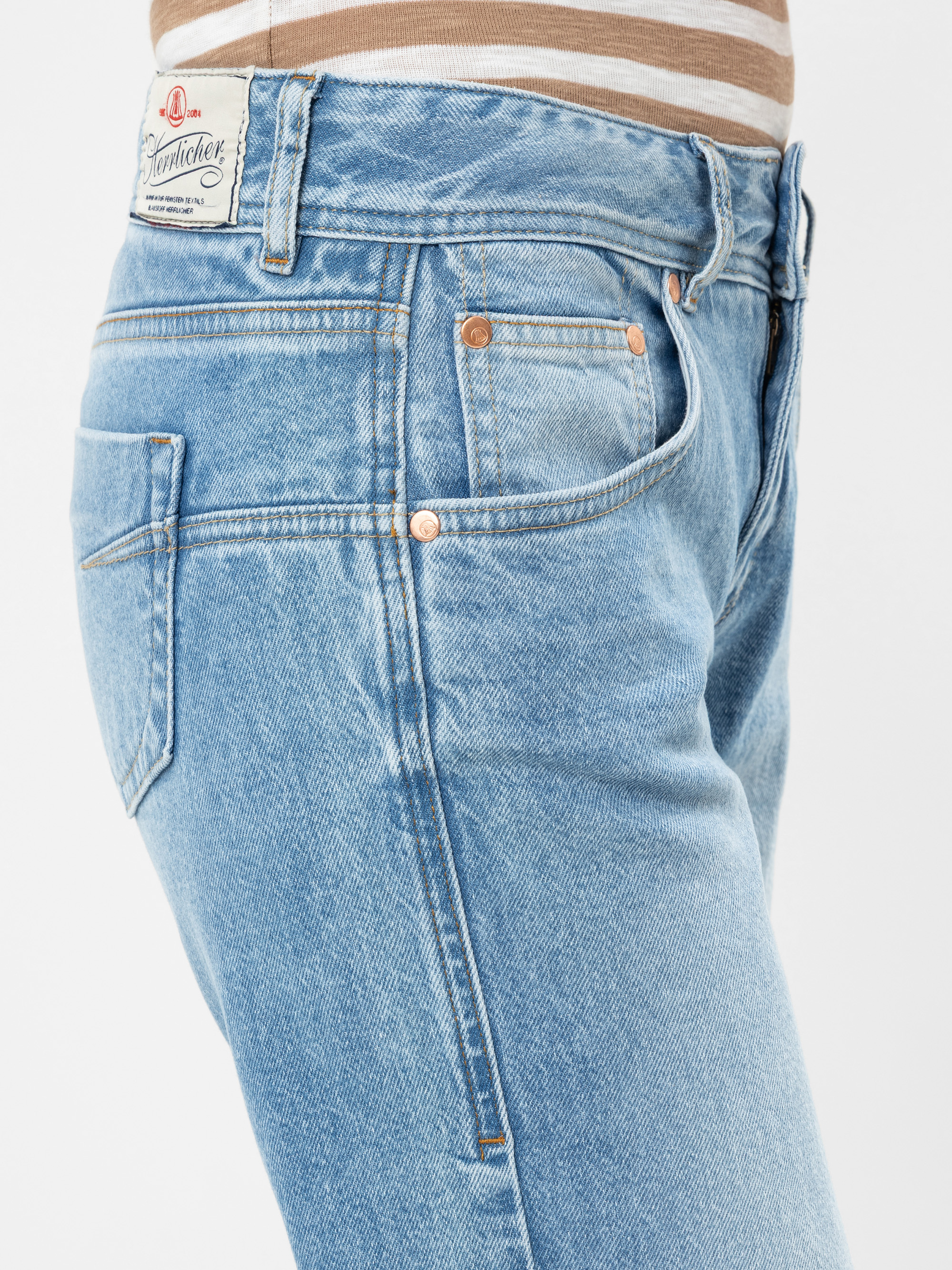 Nahaufnahme einer Person, die eine hellblaue Jeans und ein braun-weiß gestreiftes Hemd trägt, mit Details an der Rückseite der Jeans und den Seitentaschen mit sichtbaren Nähten und Nieten.