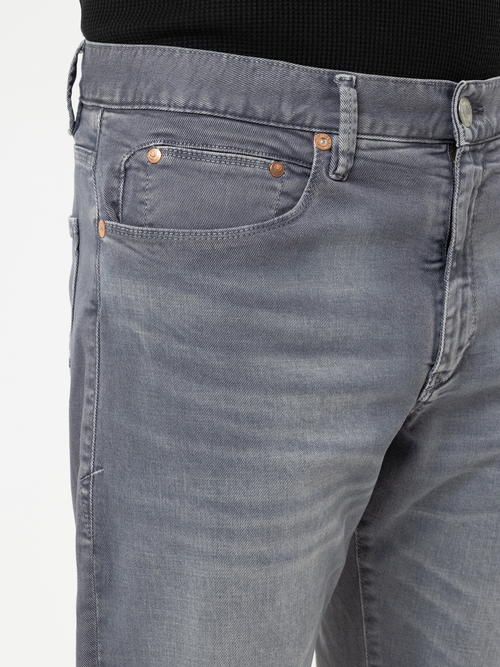 Nahaufnahme einer Person, die eine hellgraue Denim-Jeans und ein schwarzes Oberteil trägt, wobei die Vordertasche, die Gürtelschlaufen und die Metallnieten zu sehen sind.