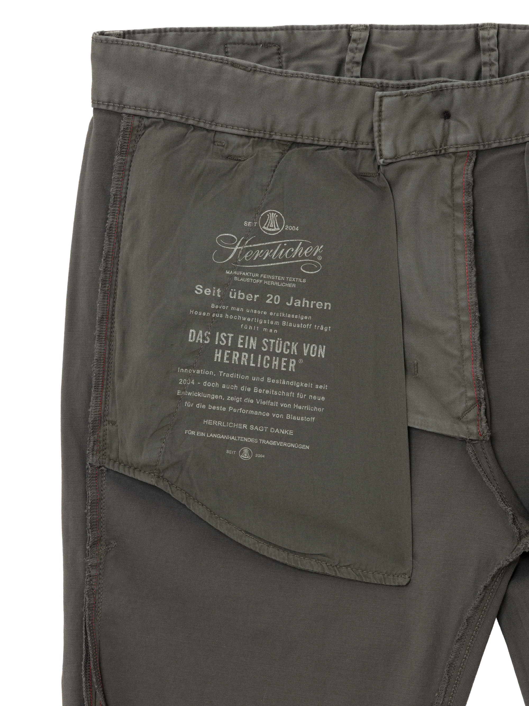 Nahaufnahme der Innenseite einer grauen Herrlicher-Hose mit dem Logo der Marke, Pflegehinweisen und einem Text in deutscher Sprache auf dem Taschenfutter.