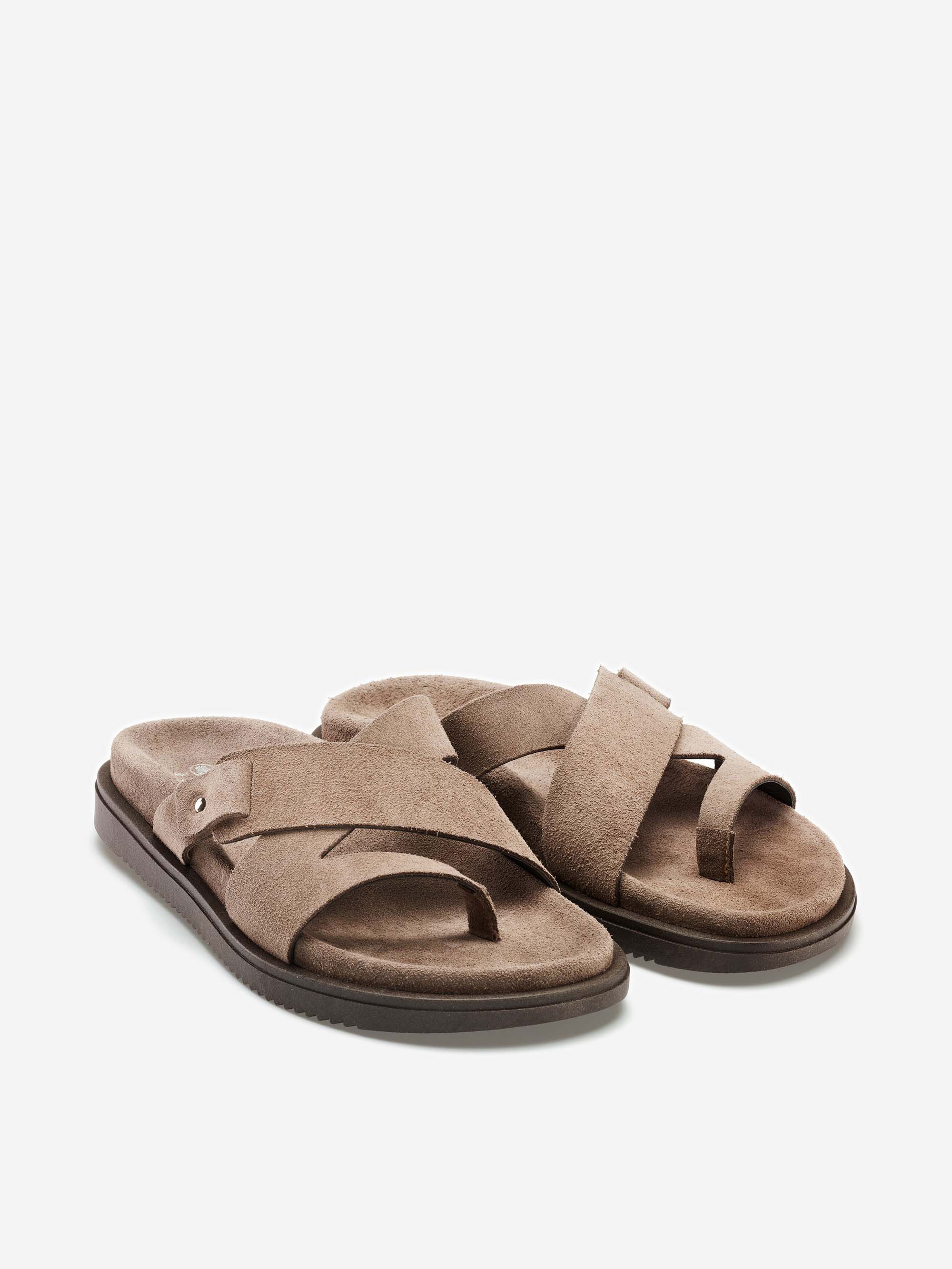 Ein Paar beigefarbene Wildleder-Sandalen mit gekreuzten Riemen, offenen Zehen und flachen dunklen Sohlen auf weißem Hintergrund.