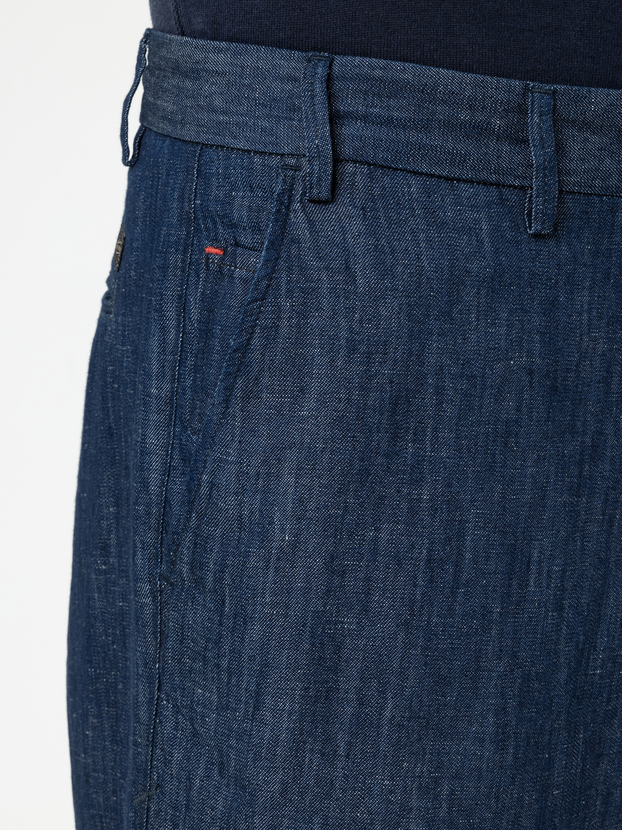 Nahaufnahme einer Person, die eine blaue Jeanshose mit einer sichtbaren Seitentasche, Gürtelschlaufen und einem Bund trägt, gepaart mit einem dunklen Hemd, das in die Hose gesteckt wird.