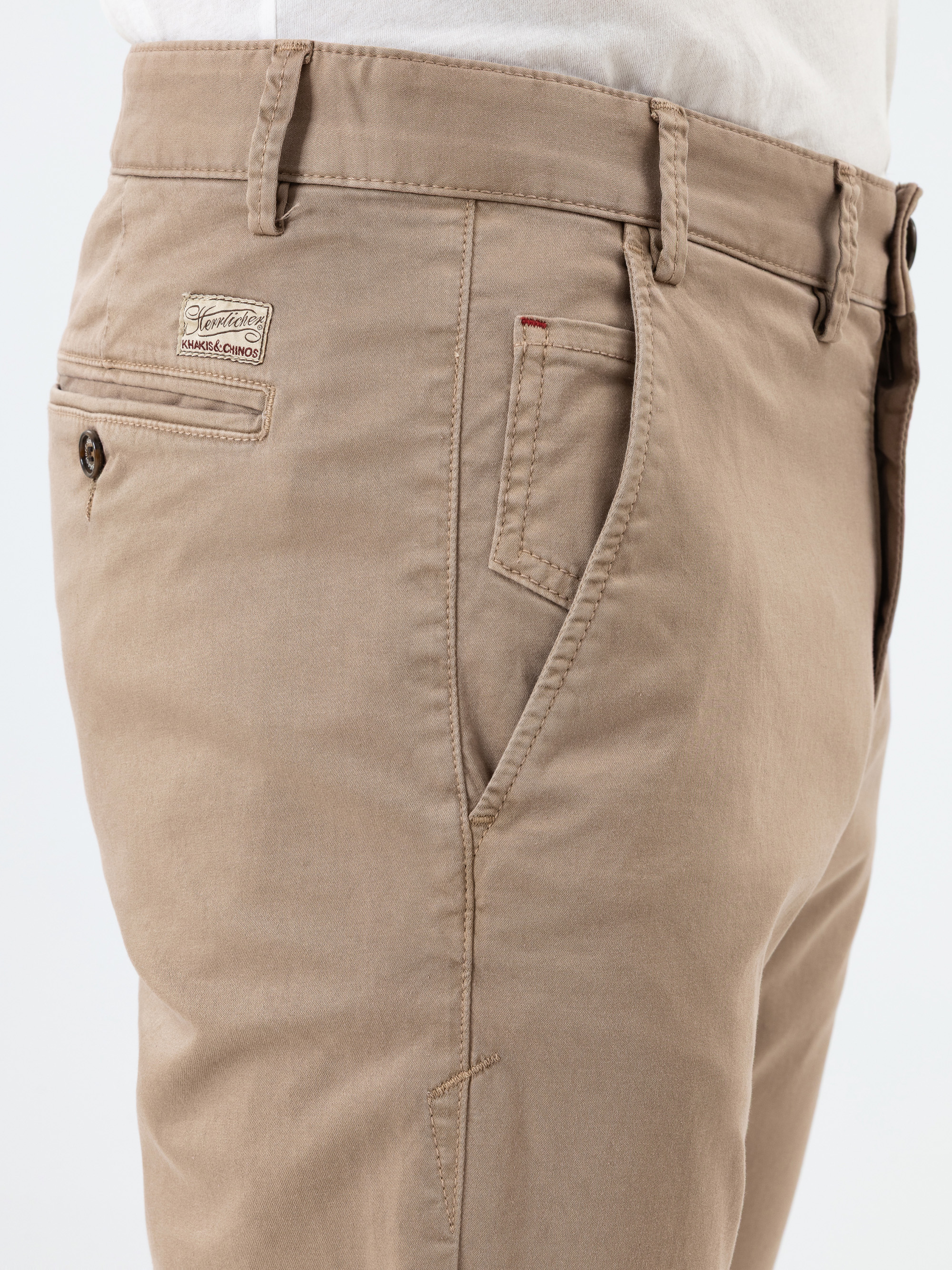 Nahaufnahme einer Person, die eine hellbraune Chino-Hose mit einem weißen Hemd in der Taille trägt. Die Hose hat eine Münztasche, eine Seitentasche, Gürtelschlaufen und einen Markenaufnäher über der rechten Tasche.