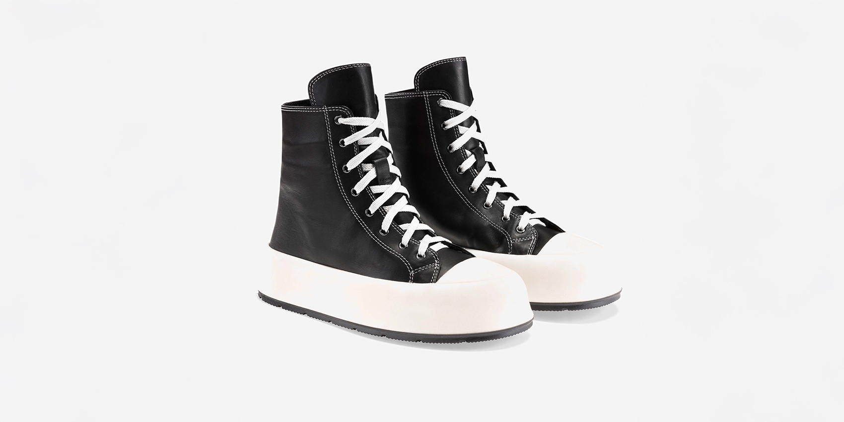 Ein Paar High-Top-Sneakers mit schwarzem Obermaterial, weißen Schnürsenkeln und dicken weißen Gummisohlen, fotografiert auf einem schlichten weißen Hintergrund.