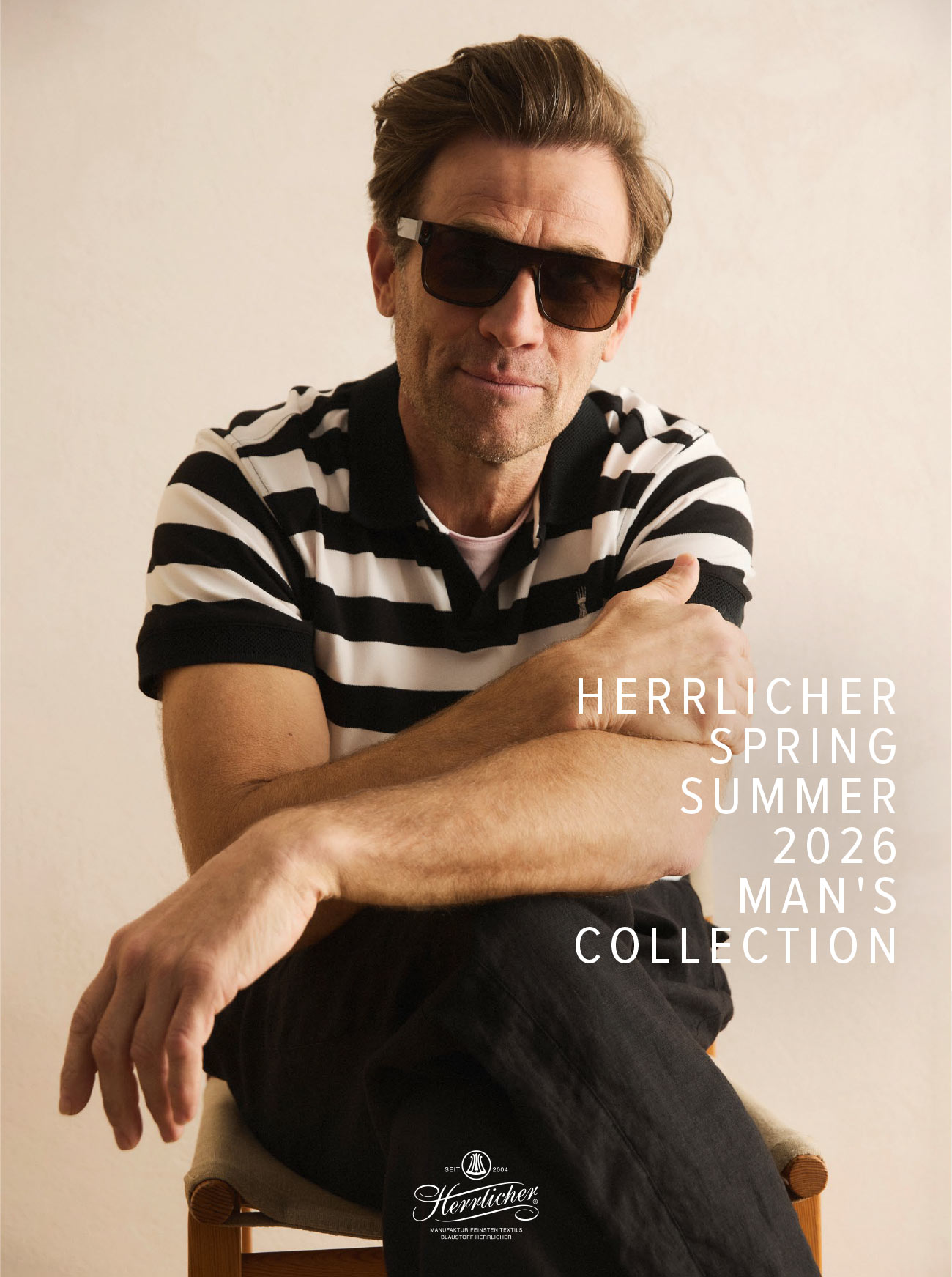 Ein Mann mit Sonnenbrille und einem schwarz-weiß gestreiften Poloshirt sitzt mit verschränkten Armen auf einem Stuhl; der Text lautet Herrlicher Spring Summer 2026 Mans Collection.