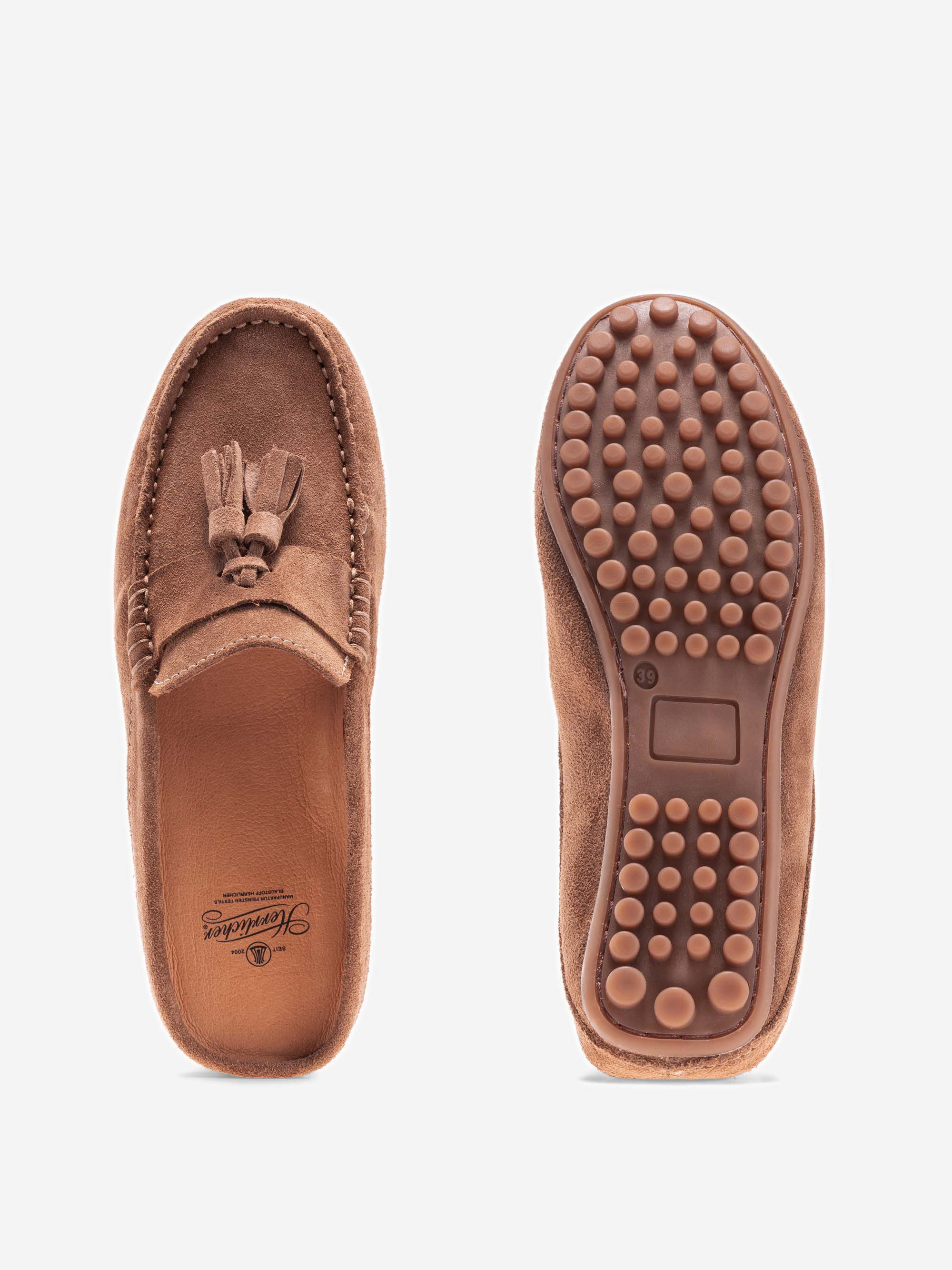Ein Paar braune Wildleder-Slipper, die von oben und unten gezeigt werden; der linke Schuh hat eine Quaste und eine gebrandete Innensohle, während der rechte Schuh eine strukturierte Gummisohle mit runden Griffen aufweist.