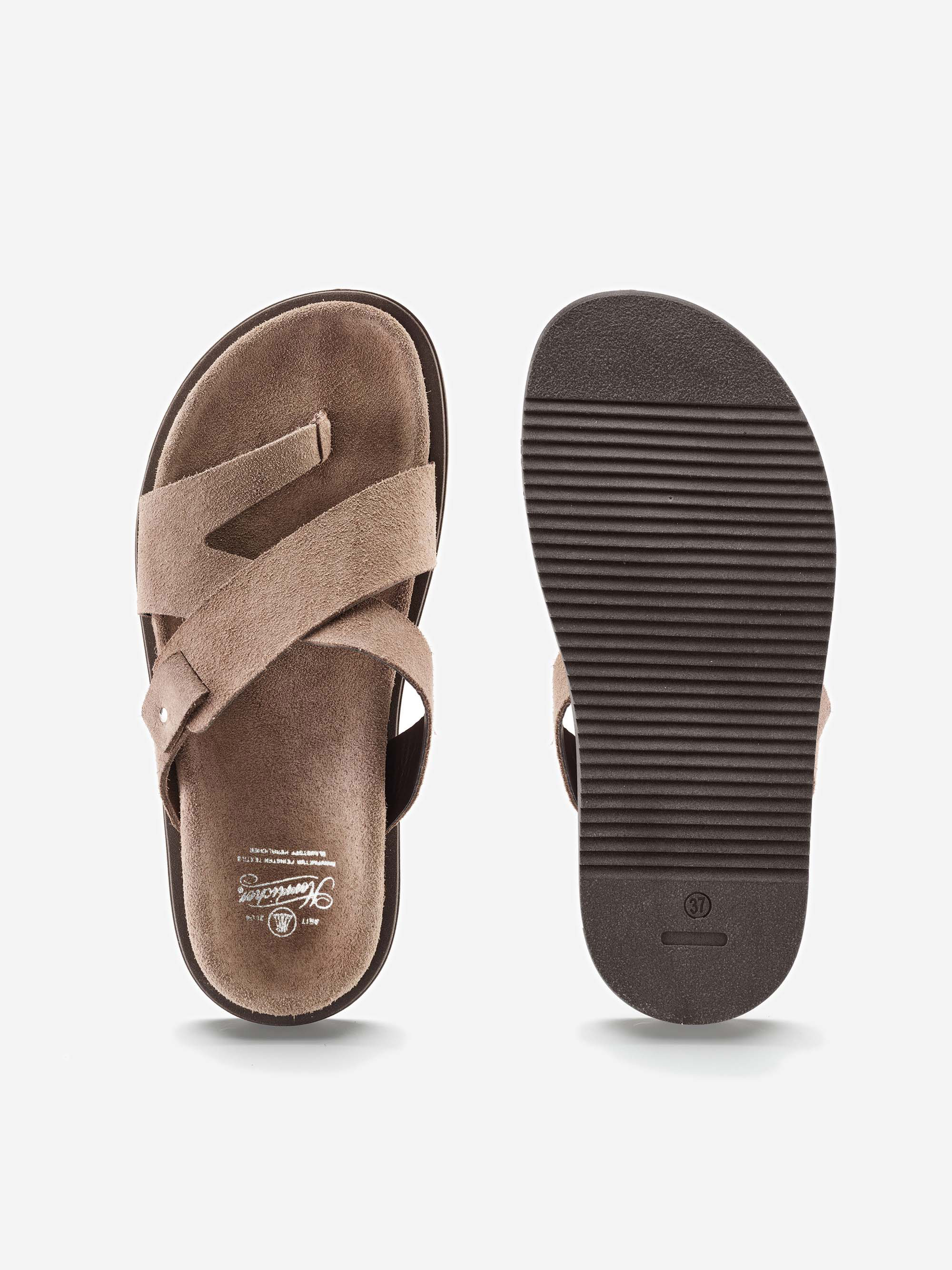 Ein Paar braune Wildleder-Sandalen, die eine zeigt das Oberteil mit gekreuzten Riemen, die andere die strukturierte Gummisohle, beide auf weißem Hintergrund.