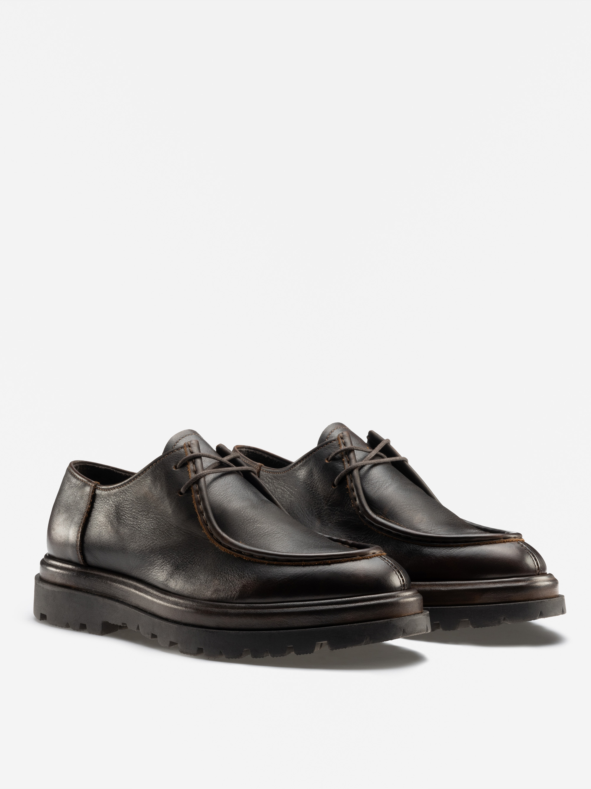 Ein Paar schwarzer Lederschnürschuhe mit dicken Gummisohlen, die auf einem schlichten weißen Hintergrund abgebildet sind. Die Schuhe haben sichtbare Nähte um den oberen Rand und ein leicht robustes, modernes Design.