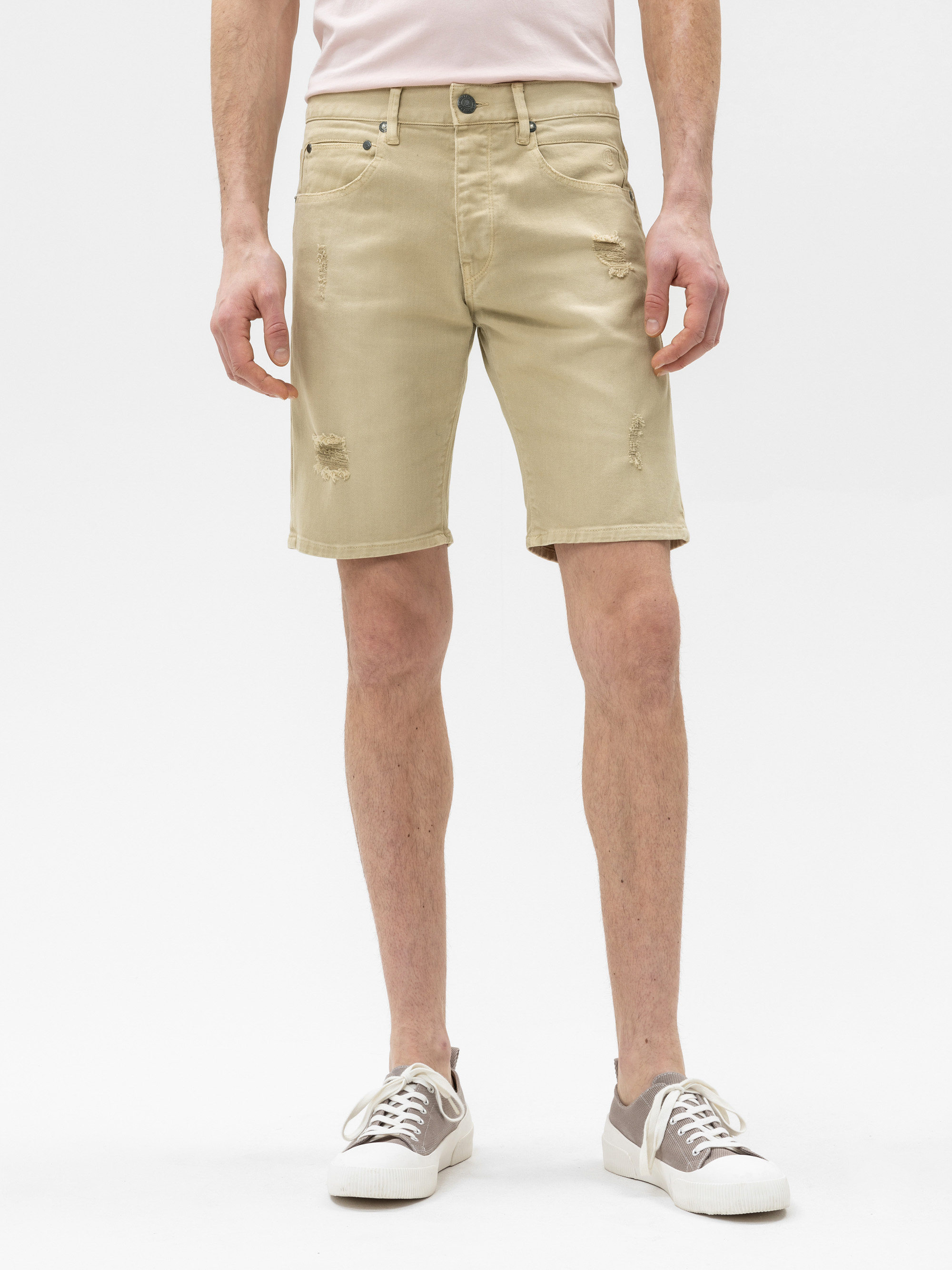 Eine Person in hellbeigen, strapazierten Jeans-Shorts und weißen Turnschuhen steht vor einem schlichten weißen Hintergrund. Die Shorts haben leichte Ausfransungen und zerrissene Details. Der Oberkörper der Person ist teilweise sichtbar.
