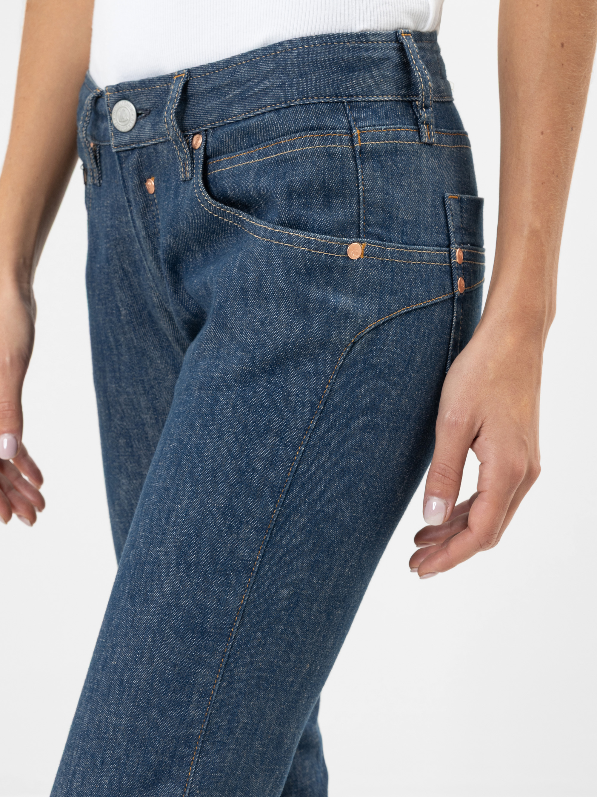 Eine Person, die Blue Denim Jeans und ein weißes Oberteil trägt, von der Taille bis zur Mitte des Oberschenkels, mit entspannten Armen an der Seite vor einem schlichten weißen Hintergrund.