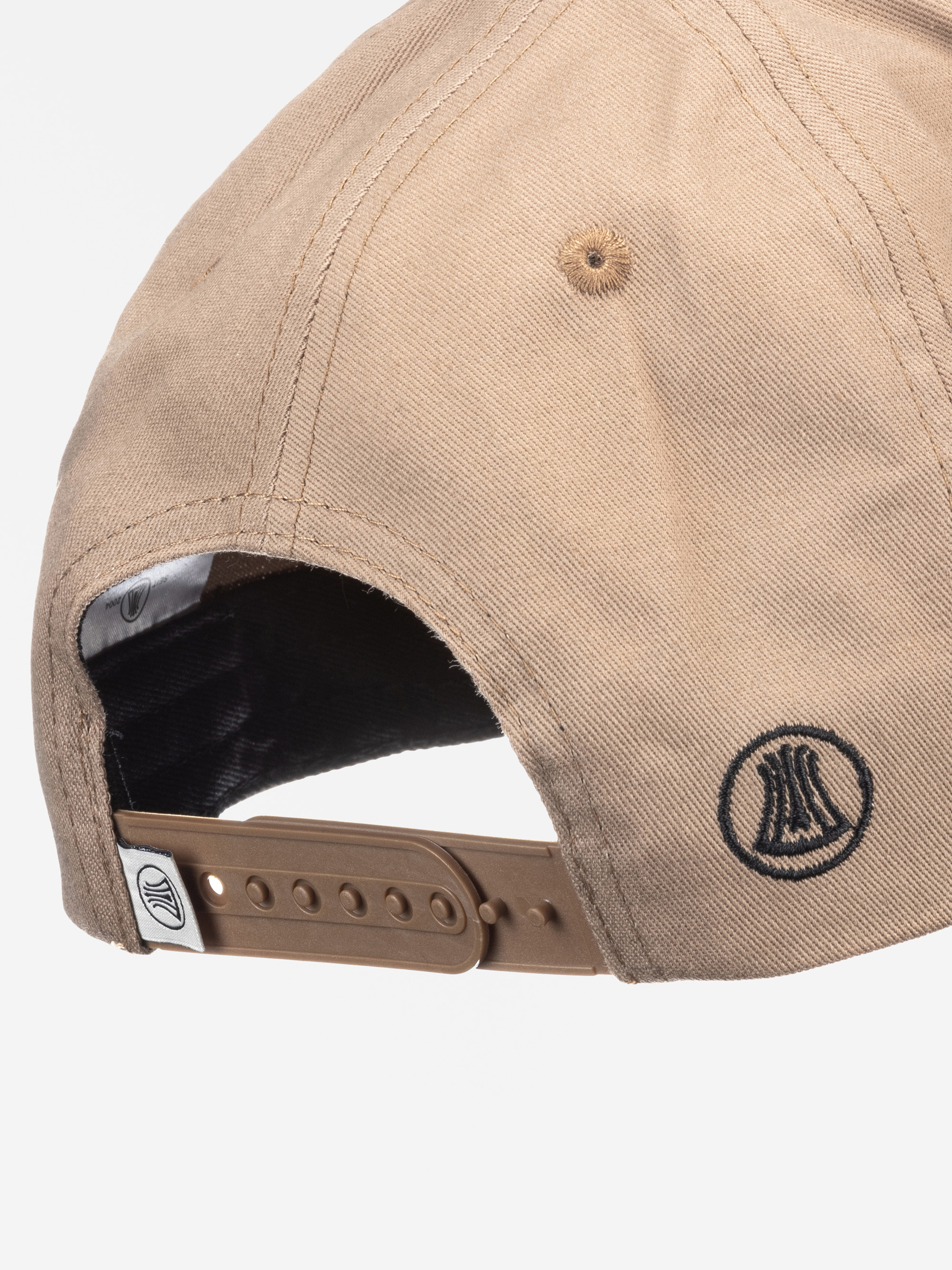 Nahaufnahme der Rückseite einer beigen Baseballmütze mit braunem verstellbarem Riemen und schwarzem gesticktem Logo. Am Riemen ist ein kleines Metallteil mit einem Logo angebracht.
