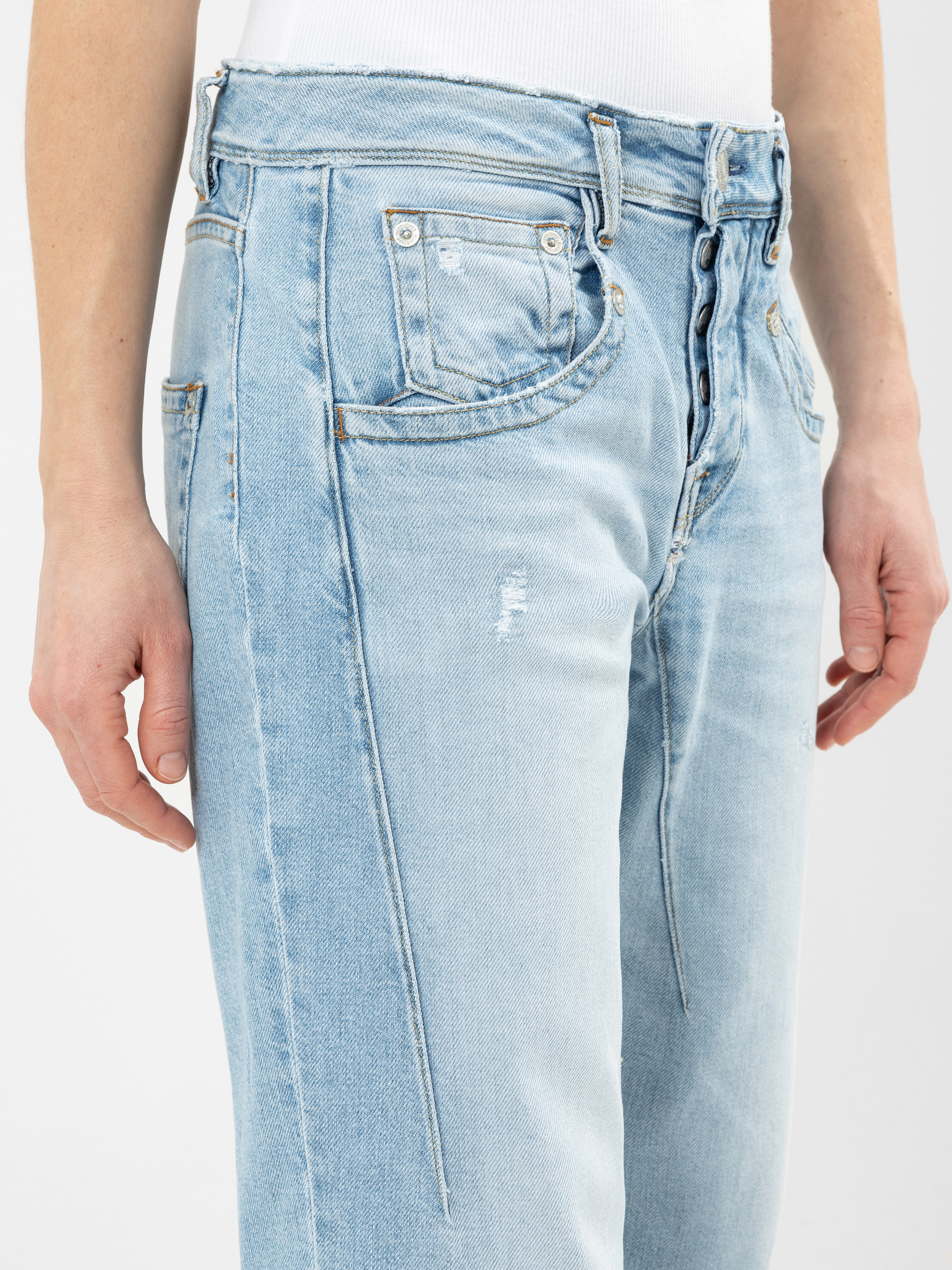 Eine Person trägt eine hellblaue, hoch taillierte Jeans mit Knopfleiste und leichten Used-Details, die Arme sind entspannt an der Seite ausgestreckt. Die Jeans hat Seitentaschen und vertikale Nahtakzente.