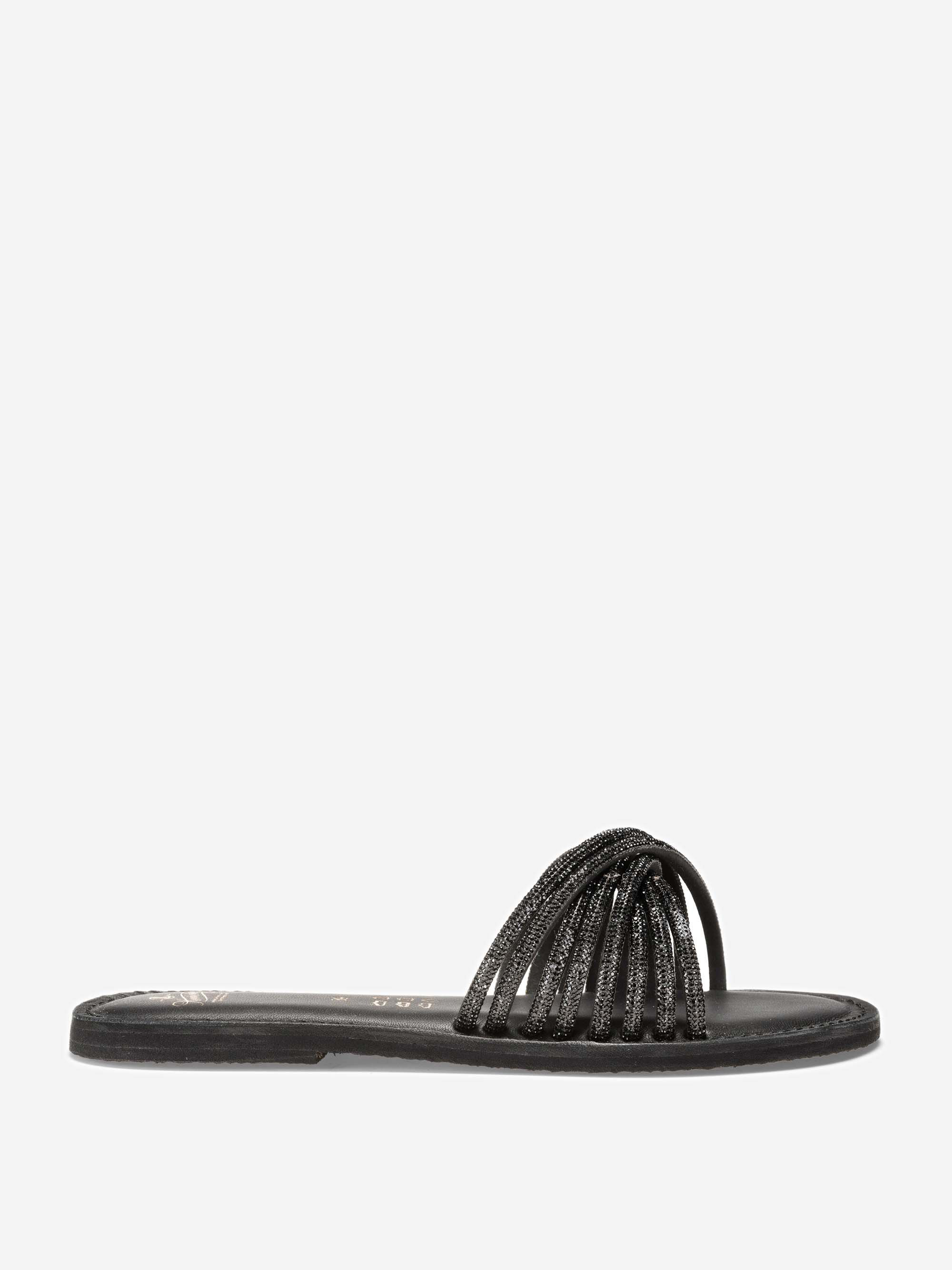 Eine schwarze flache Sandale mit offener Spitze und mehreren dünnen, glitzernden Riemen, die sich über die Vorderseite wölben, vor einem schlichten weißen Hintergrund.