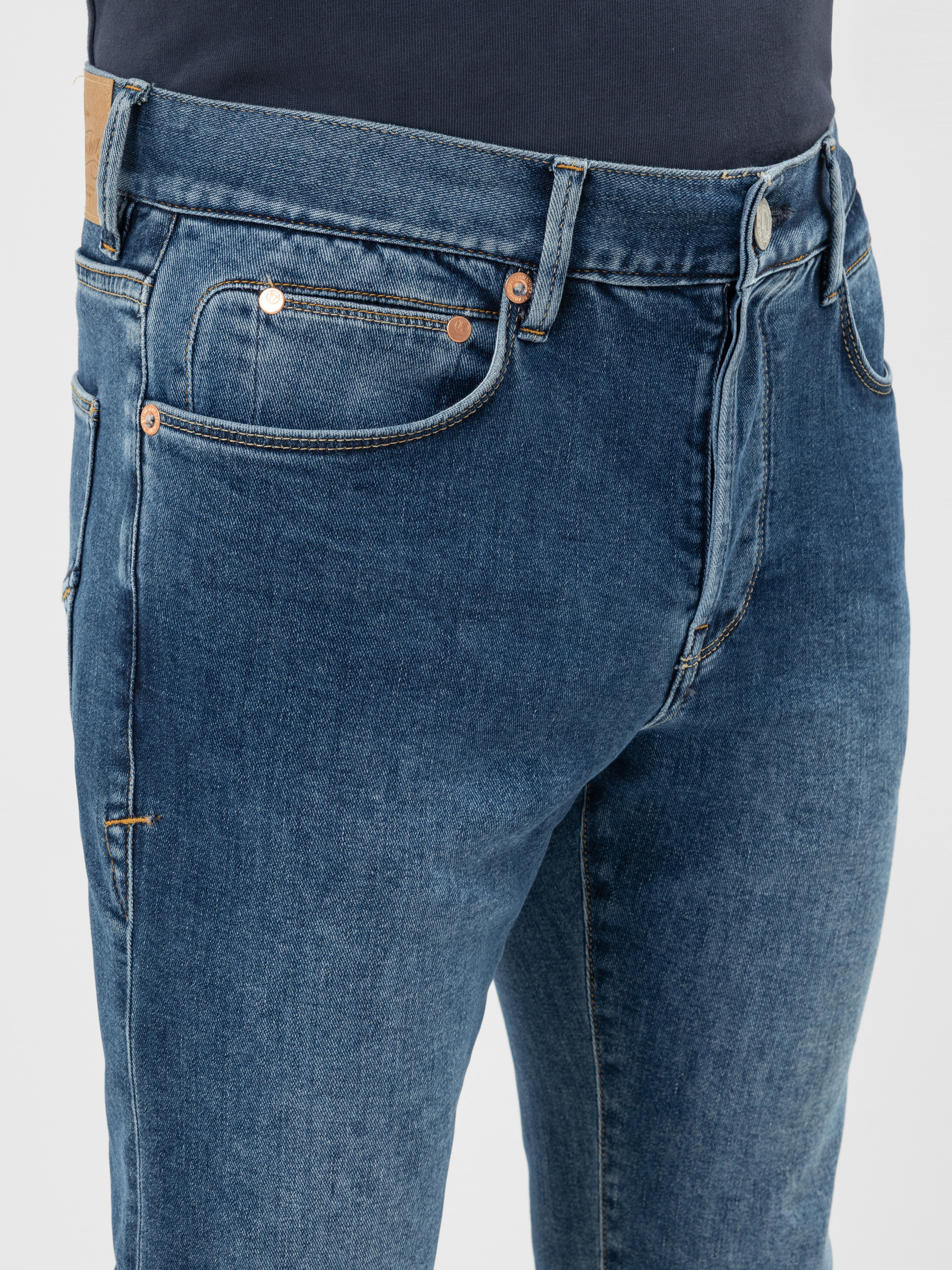 Nahaufnahme einer Person, die Blue Denim Jeans und ein dunkles Hemd trägt. Die Jeans hat Kupfernieten, einen Knopf auf der Vorderseite, sichtbare Nähte und ein klassisches Five-Pocket-Design.