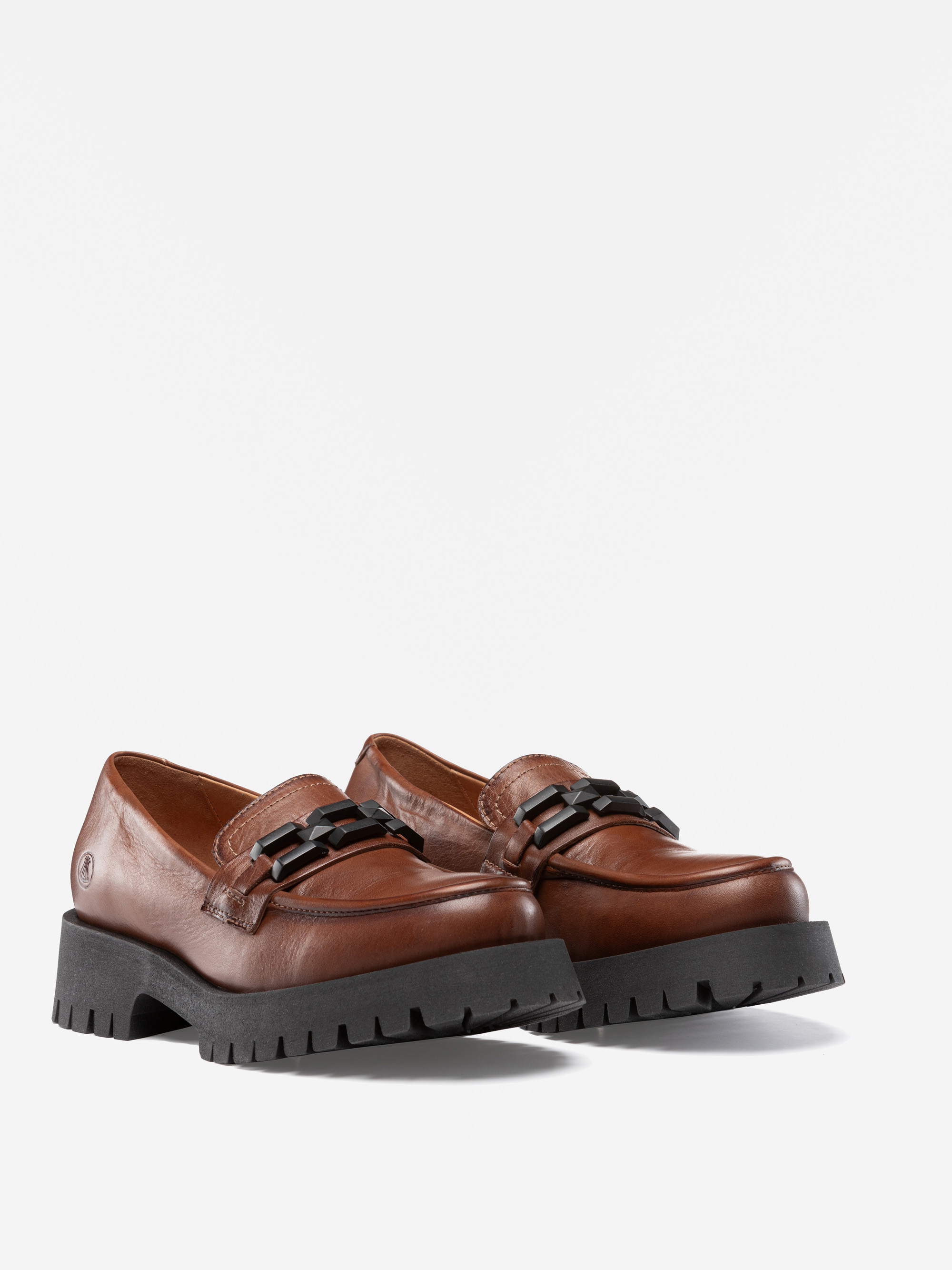 Ein Paar braune Leder-Slipper mit klobigen schwarzen Gummisohlen und dekorativen schwarzen Kettendetails auf dem Oberteil, dargestellt auf einem weißen Hintergrund.