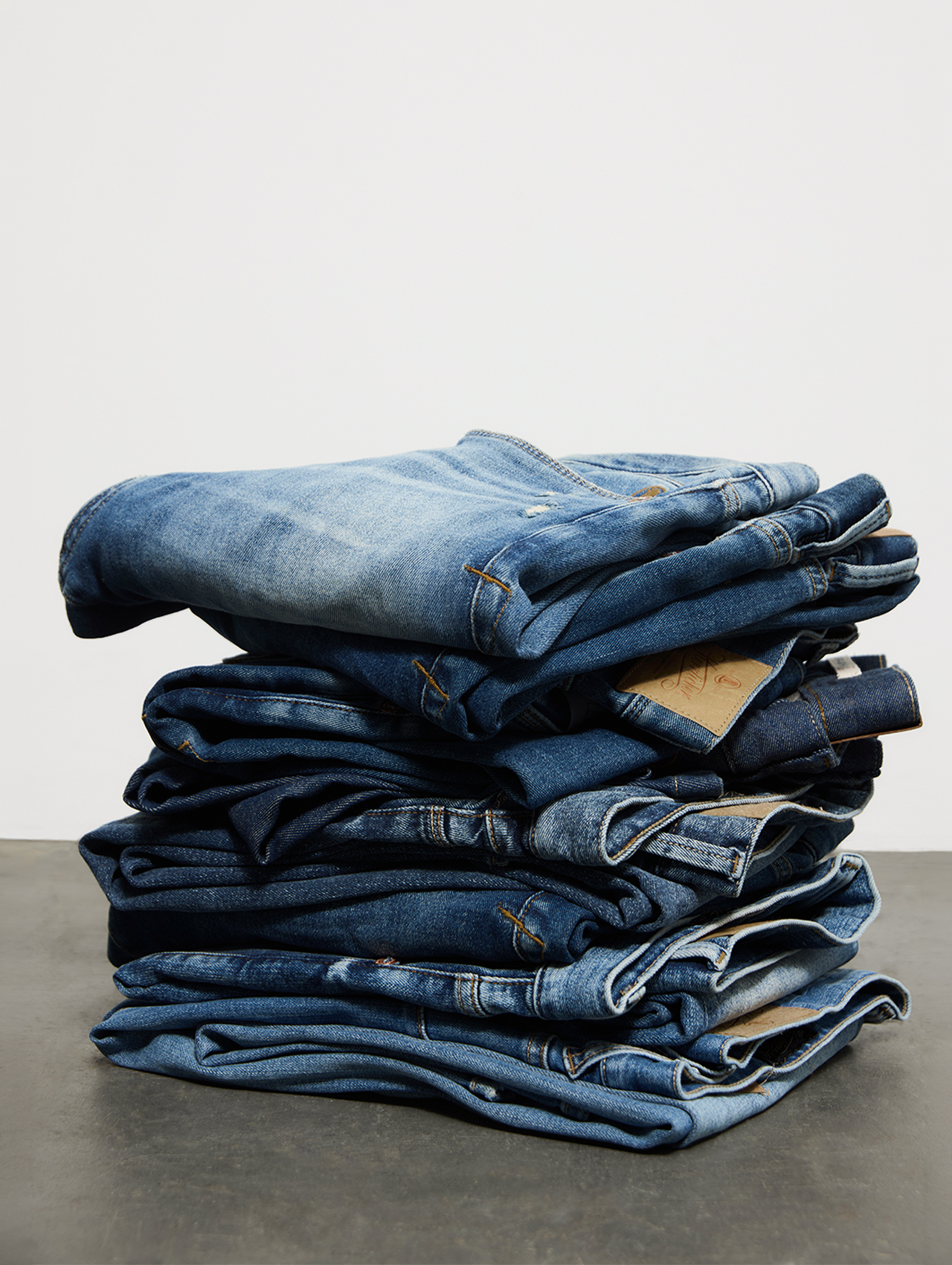 Auf einer dunkelgrauen Fläche vor einem schlichten weißen Hintergrund liegt ein Stapel ordentlich gefalteter Bluejeans in verschiedenen Waschungen.