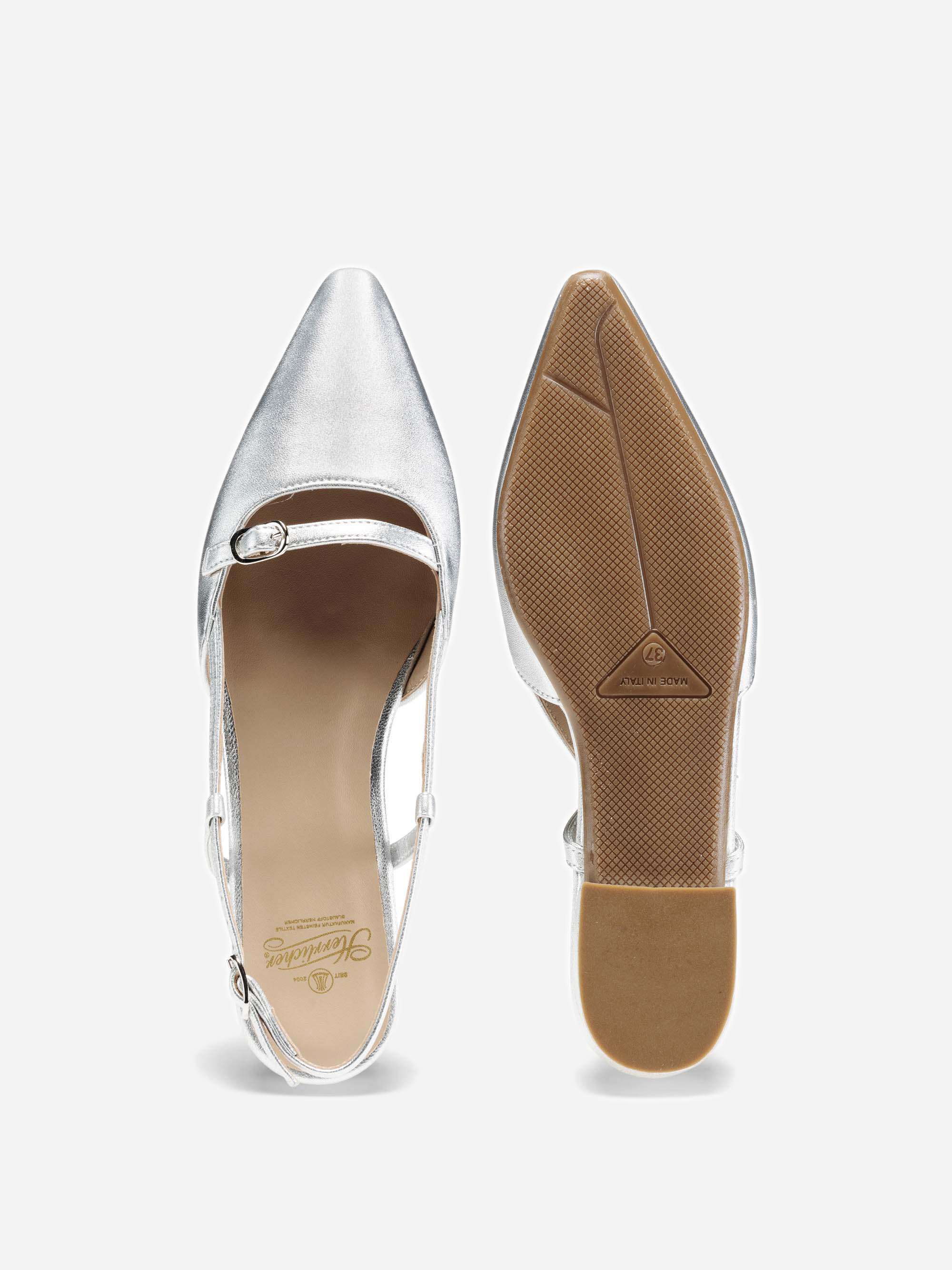 Ein Paar spitz zulaufende silberne Kleiderschuhe mit niedrigem Absatz, Knöchelriemen und Schnalle, die sowohl von oben als auch von unten auf einem schlichten weißen Hintergrund gezeigt werden.
