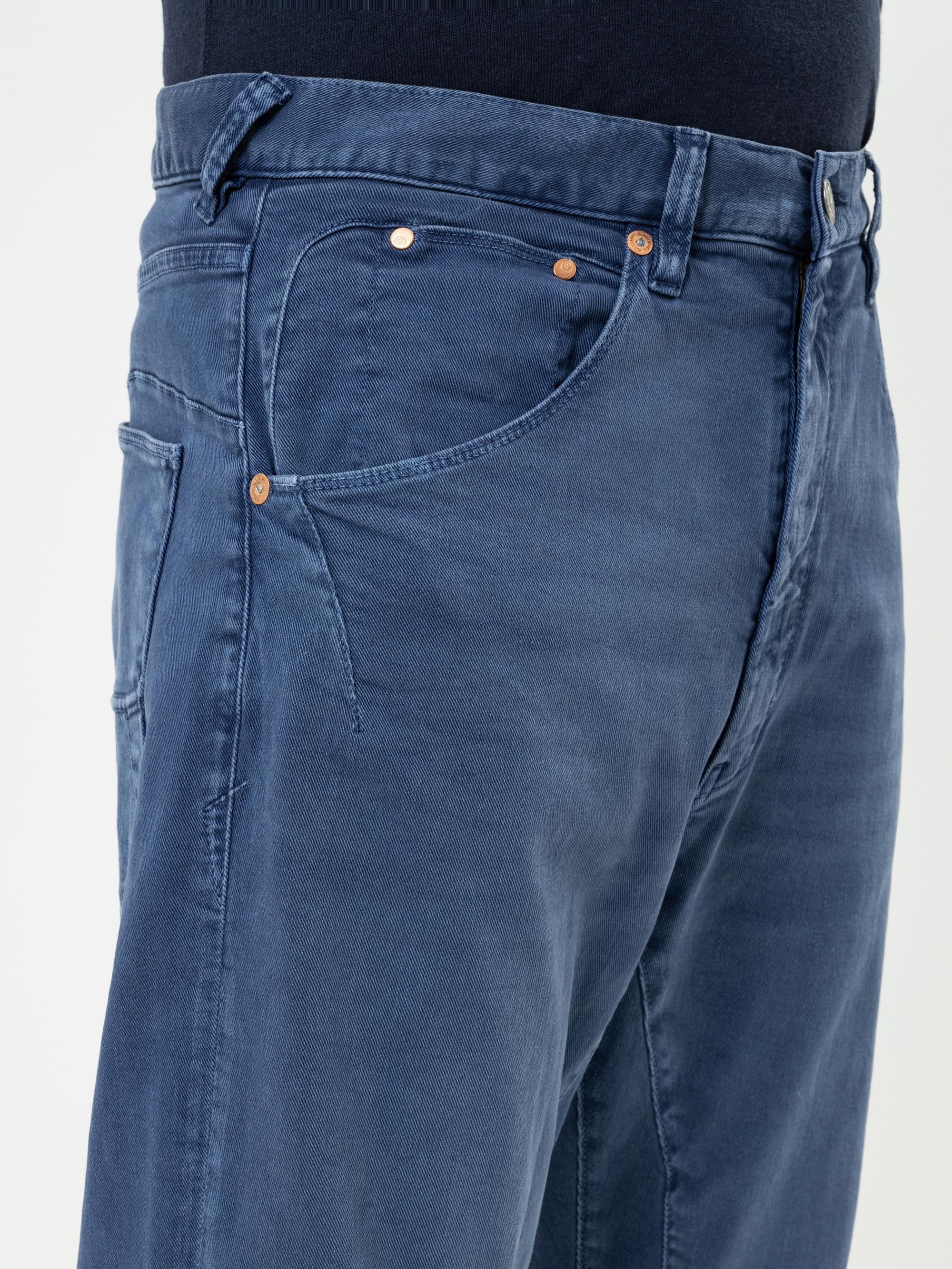 Nahaufnahme einer Person, die eine blaue Jeans und ein dunkles Hemd trägt. Man sieht die Vordertasche, den Knopf und einen Teil der Gürtelschlaufen.