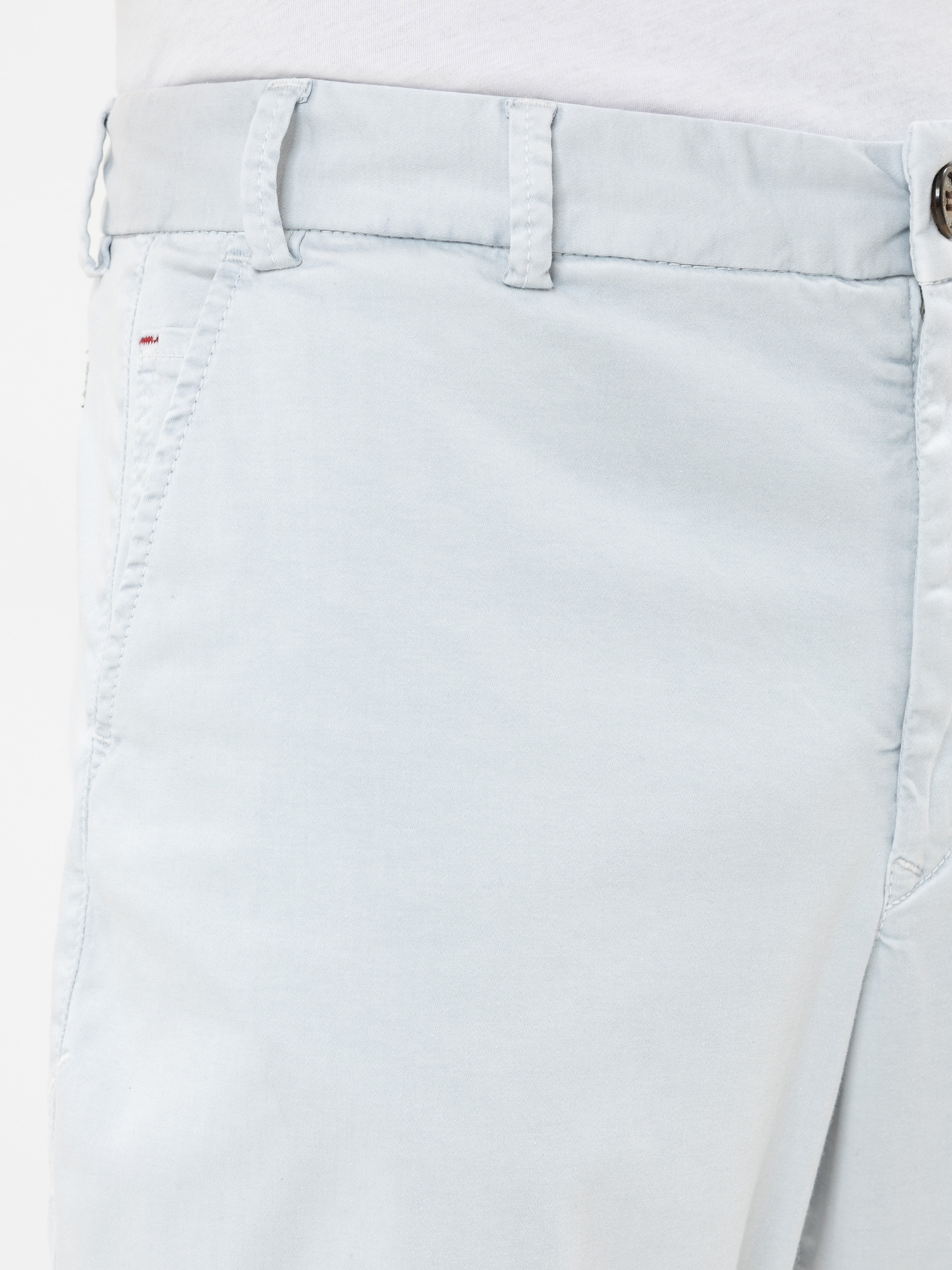 Nahaufnahme einer Person, die eine hellblaue Hose mit einer sichtbaren Vordertasche, Gürtelschlaufen und einem Knopfverschluss trägt. Die Hose wird mit einem weißen Hemd kombiniert, das in der Taille gesteckt wird.