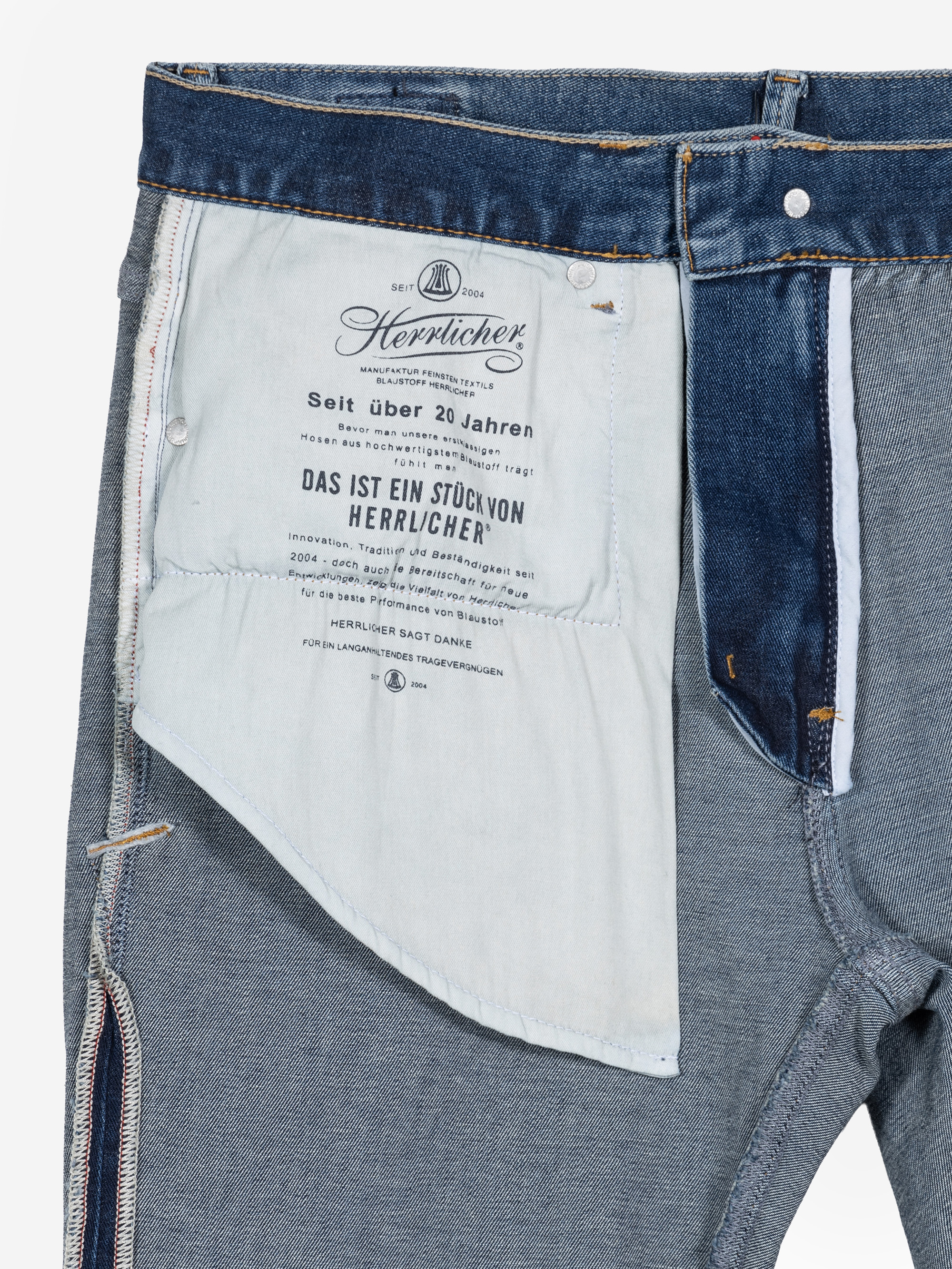 Nahaufnahme der Innenseite einer Jeans, die den Bereich der Innentasche mit aufgedrucktem deutschen Text, sichtbare Nähte und Details des Jeansstoffs zeigt. Die Jeans ist teilweise auf links gedreht, um das Innendesign zu zeigen.