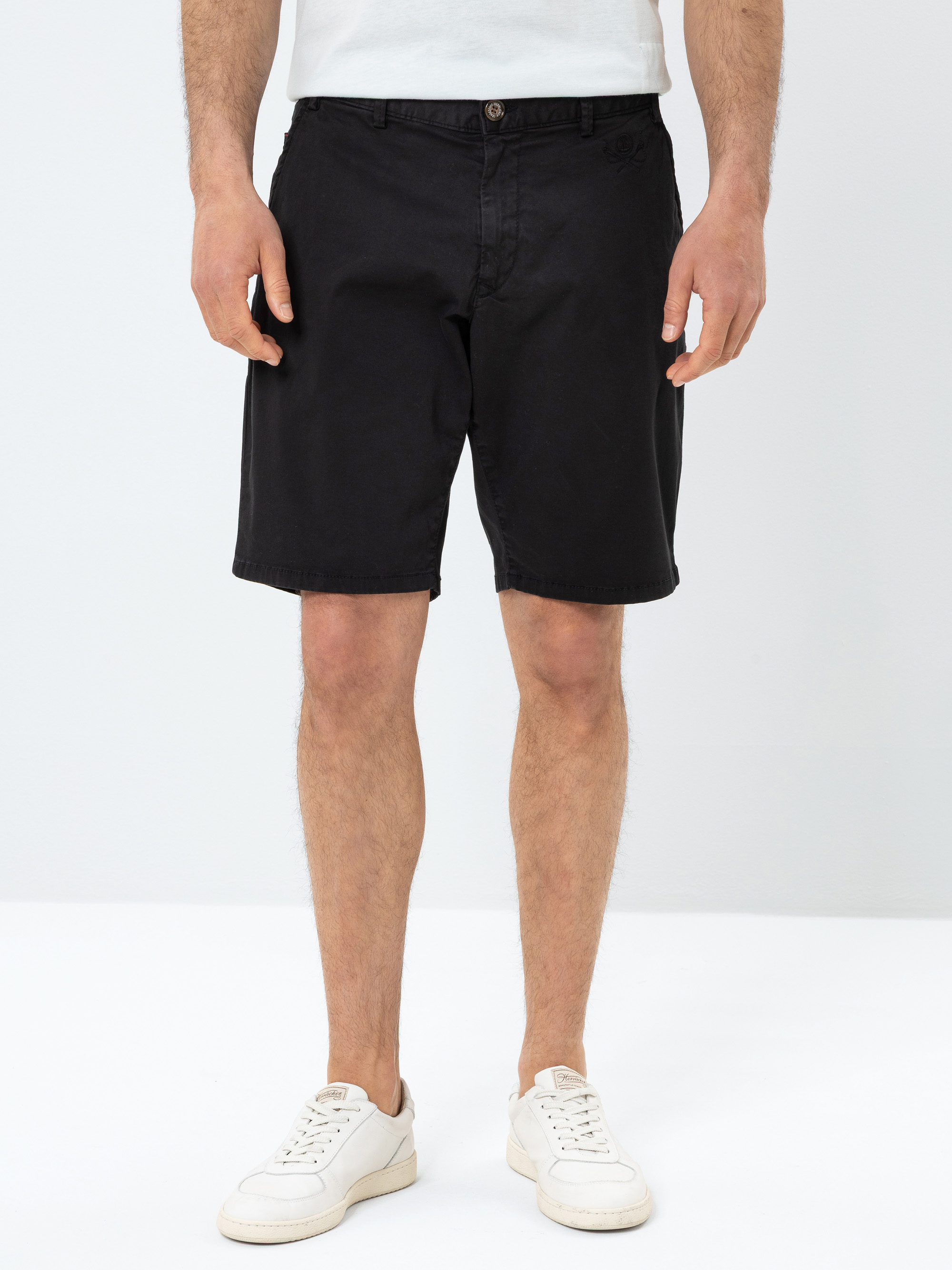 Eine Person, die ein weißes T-Shirt, schwarze knielange Shorts und weiße Turnschuhe trägt, steht vor einem schlichten weißen Hintergrund.