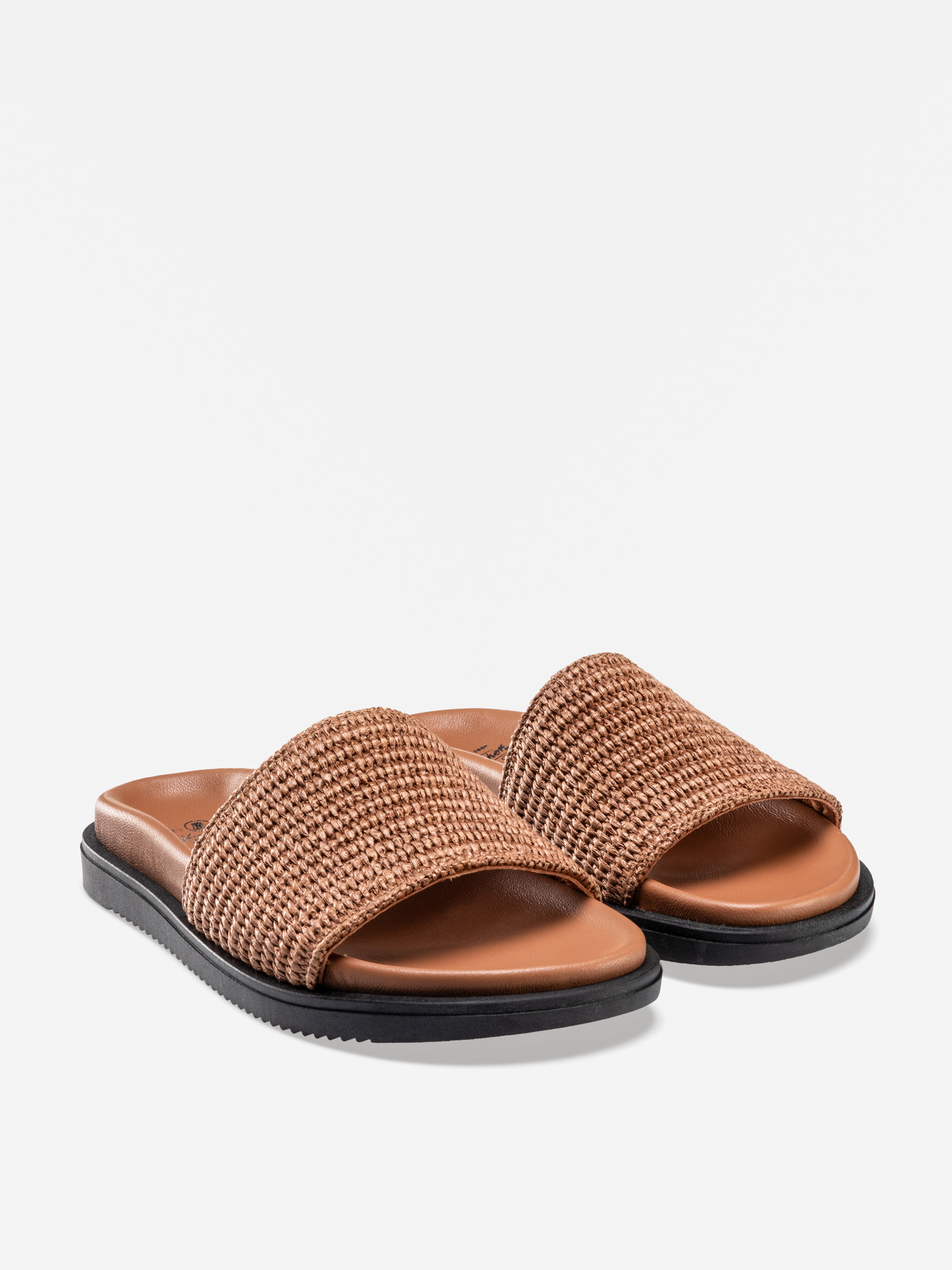 Ein Paar brauner, gewebter Slide-Sandalen mit breiten, strukturierten Riemen, braunem, gepolstertem Fußbett und schwarzer, flacher Sohle, dargestellt auf weißem Hintergrund.