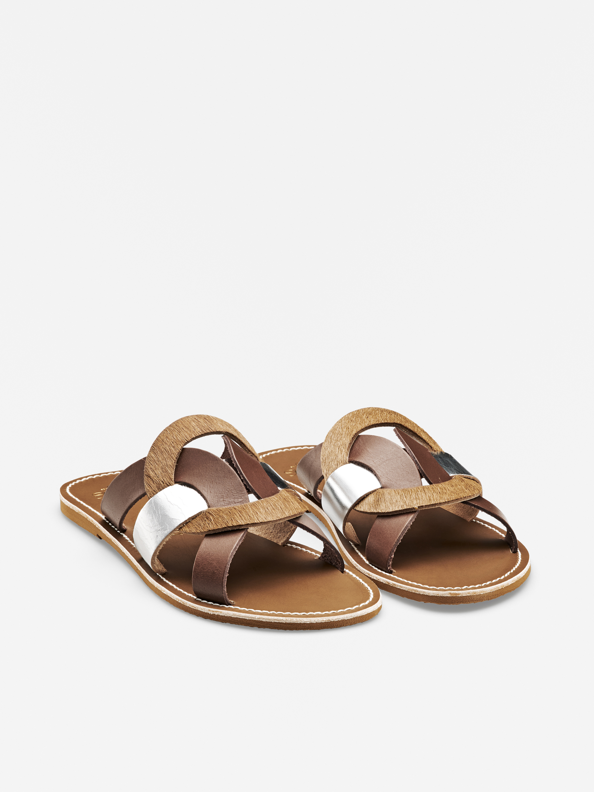 Ein Paar flache, zehenoffene Sandalen mit überkreuzten Riemen in den Farben Braun, Hellbraun und Silbermetallic auf einem schlichten weißen Hintergrund.