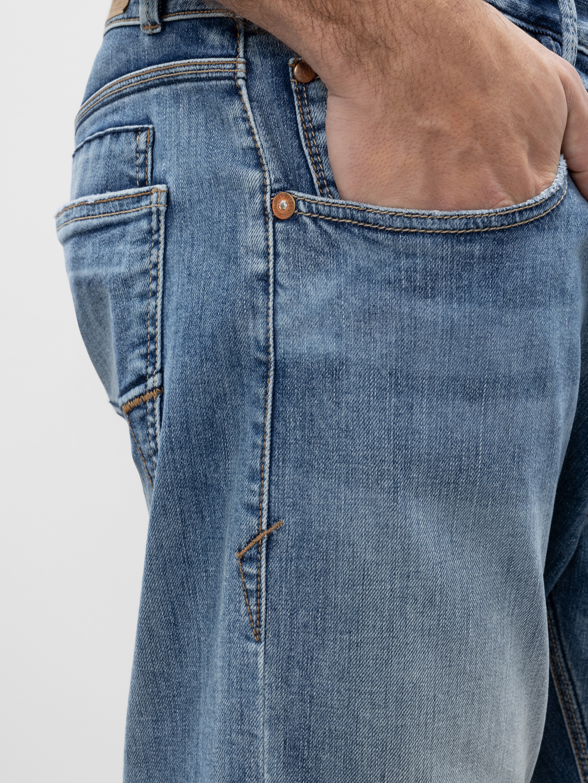 Nahaufnahme einer Person, die eine blaue Jeans trägt und ihre rechte Hand in die Vordertasche steckt. Die Jeans hat sichtbare Nähte und Metallnieten.