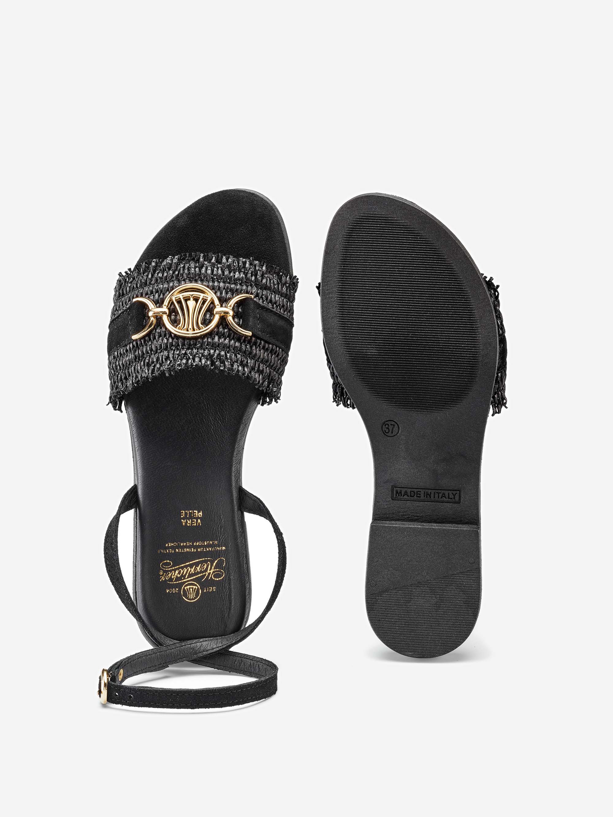 Ein Paar schwarze, zehenoffene Sandalen mit gewebten Details, goldenen dekorativen Akzenten auf dem vorderen Riemen und Knöchelriemen. Eine Sandale ist von oben und die andere von unten gezeigt, wobei die Sohle zu sehen ist.