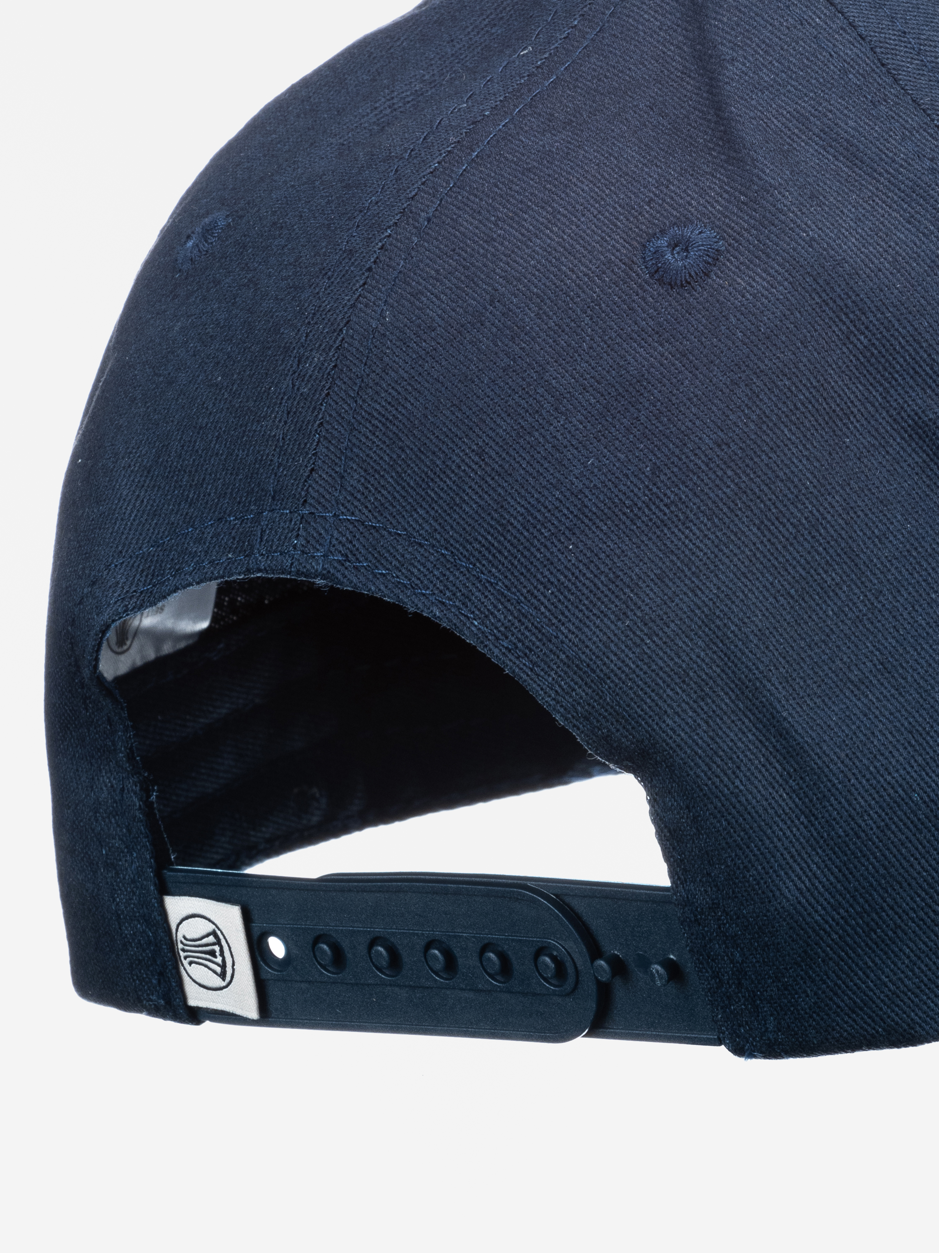 Nahaufnahme der Rückseite einer marineblauen Baseballmütze mit verstellbarem Snapback-Riemen und einem kleinen Metallemblem mit stilisiertem Wellenmuster.