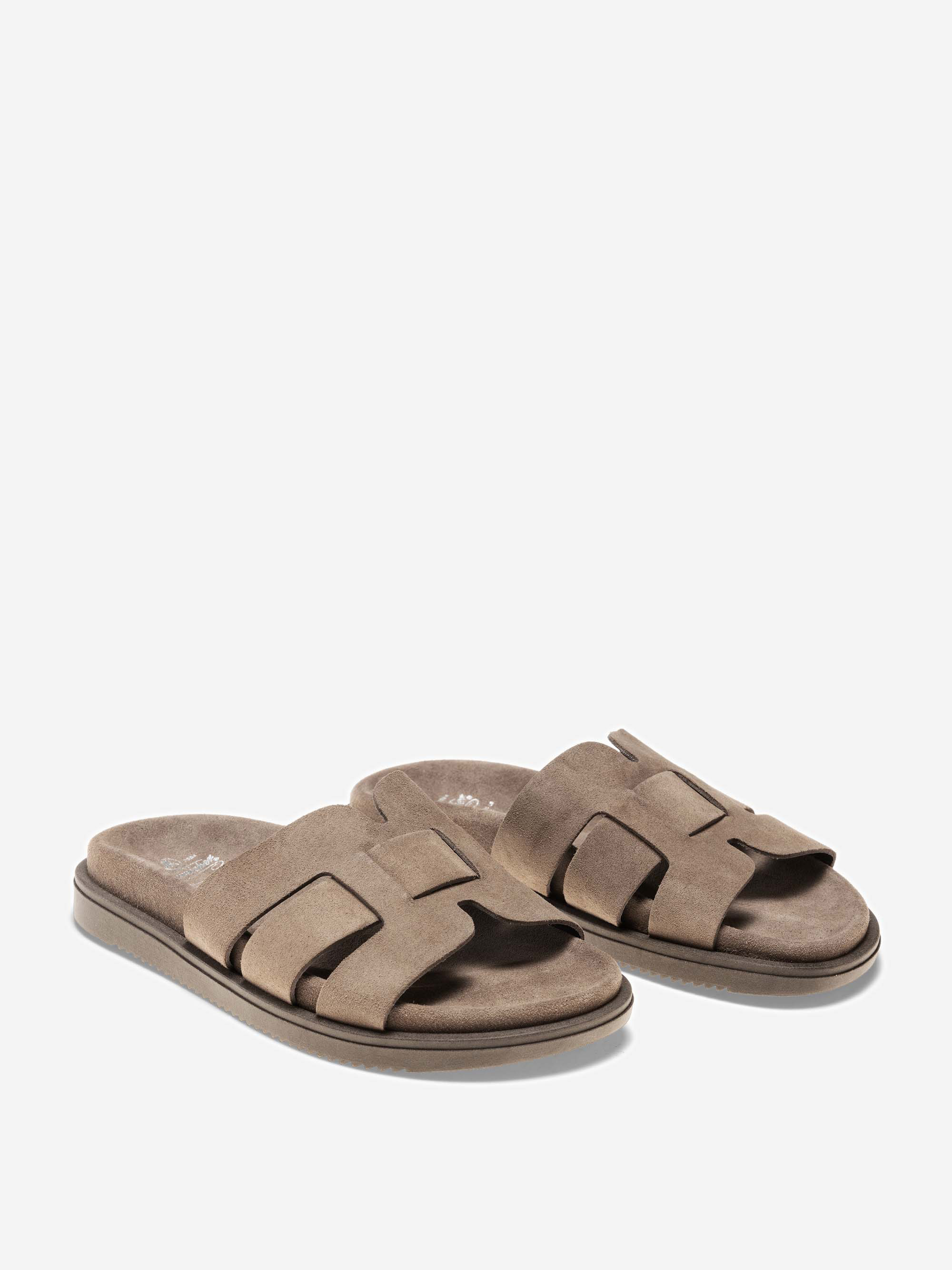 Ein Paar taupefarbene Wildleder-Sandalen mit breiten, überlappenden Riemen und flachen Sohlen auf weißem Hintergrund.