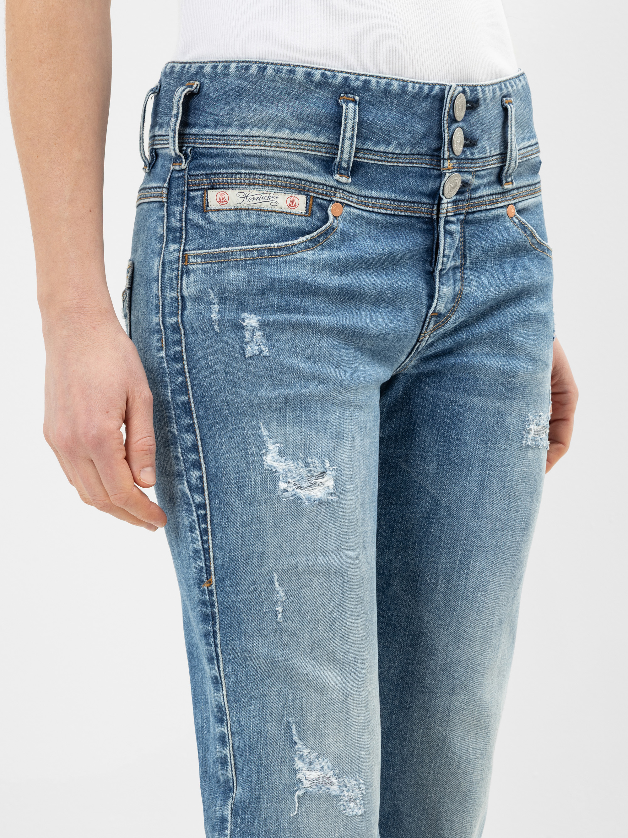 Eine Person, die eine hellblaue Jeans mit dreifachem Knopfverschluss und ein weißes Oberteil trägt; die Jeans hat sichtbare Risse und verblasste Stellen.