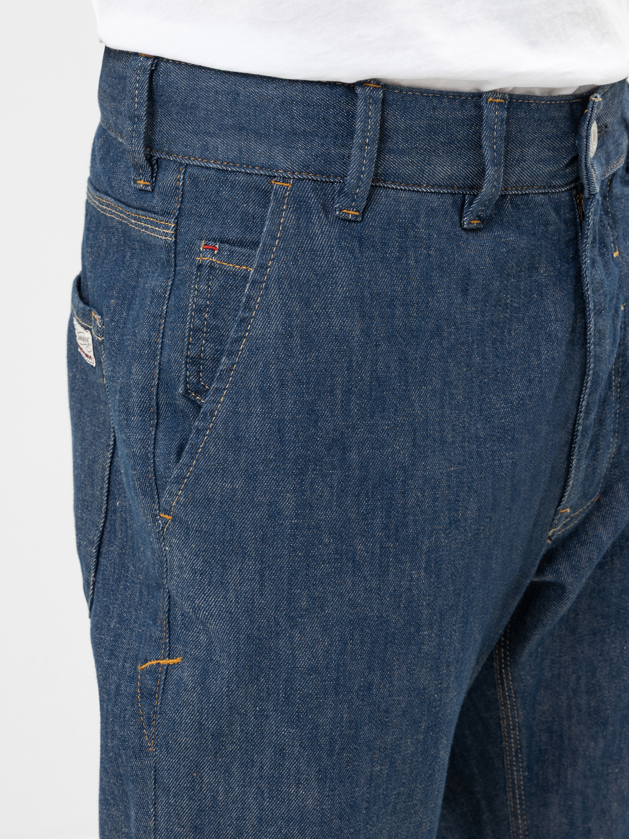 Nahaufnahme einer Person, die Blue Denim Jeans und ein weißes Hemd trägt. Das Bild konzentriert sich auf die Oberseite der Jeans und zeigt Vorder- und Seitentaschen, Gürtelschlaufen und Nähte.