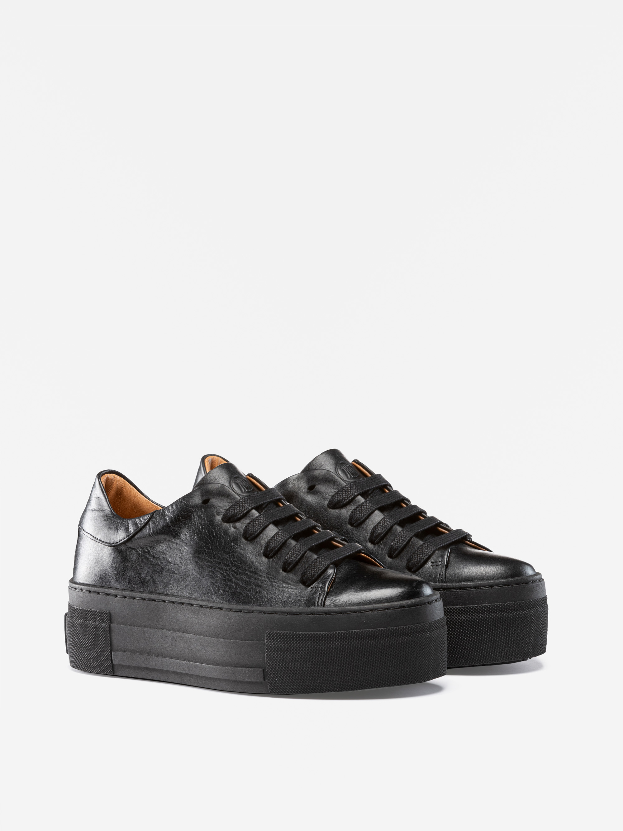 Ein Paar schwarze Plateau-Sneakers aus Leder mit schwarzen Schnürsenkeln und dicken schwarzen Sohlen, die vor einem schlichten weißen Hintergrund stehen.