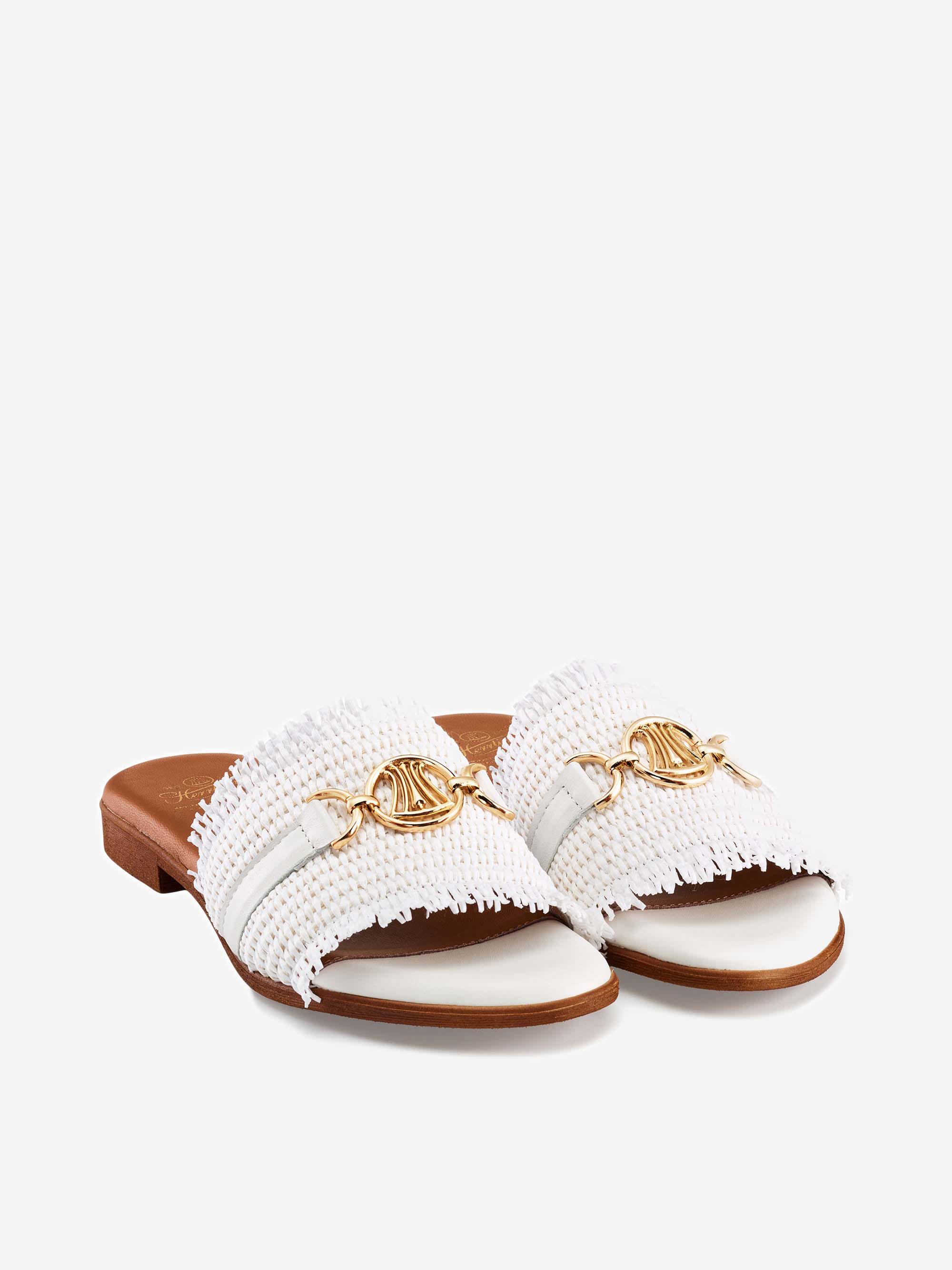 Ein Paar eleganter weißer flacher Slide-Sandalen mit ausgefransten Stoffriemen, goldenen Kettendetails und hellbraunen Sohlen, die auf einem schlichten weißen Hintergrund präsentiert werden.