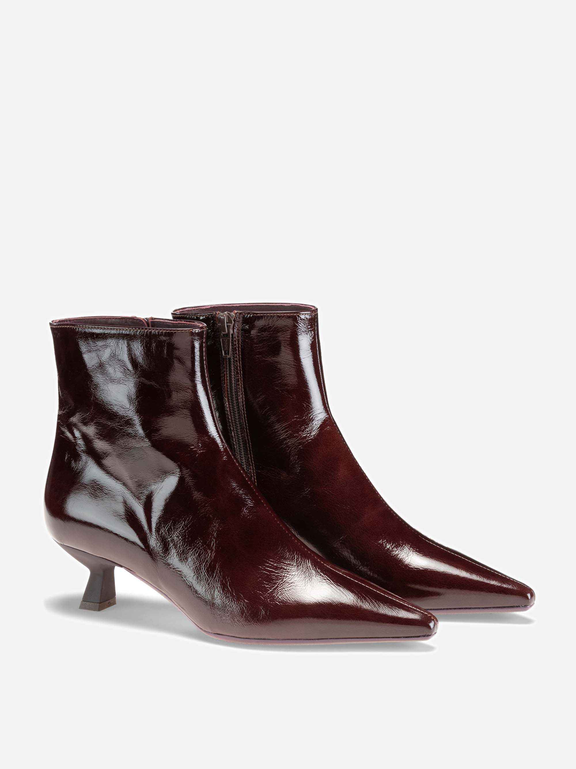 Ein Paar glänzender, weinroter Stiefeletten mit spitzen Zehen, niedrigem Kitten-Heel und seitlichen Reißverschlüssen auf hellem Hintergrund.