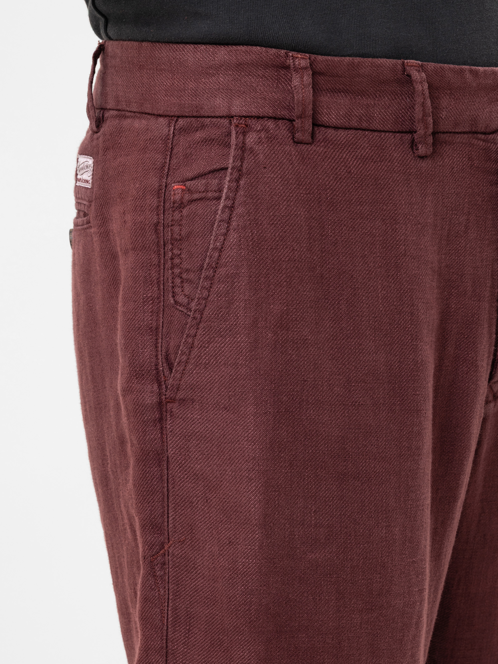 Nahaufnahme einer Person, die eine kastanienbraune Jeans mit sichtbaren Gürtelschlaufen, Taschennähten und einem Teil eines schwarzen Hemdes trägt, das in der Taille gesteckt ist.