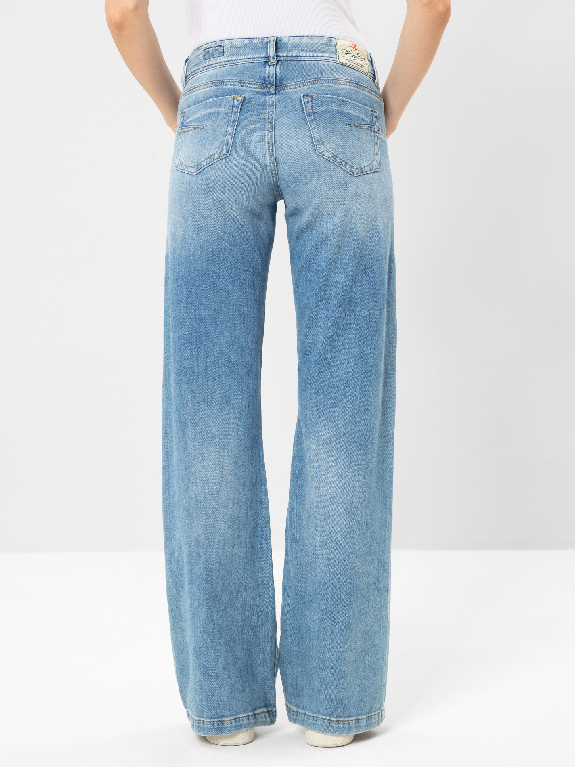 Rückenansicht einer Person, die eine hellblaue, hoch taillierte Jeans mit weitem Bein und zwei Gesäßtaschen trägt; die Person steht vor einem schlichten hellen Hintergrund.