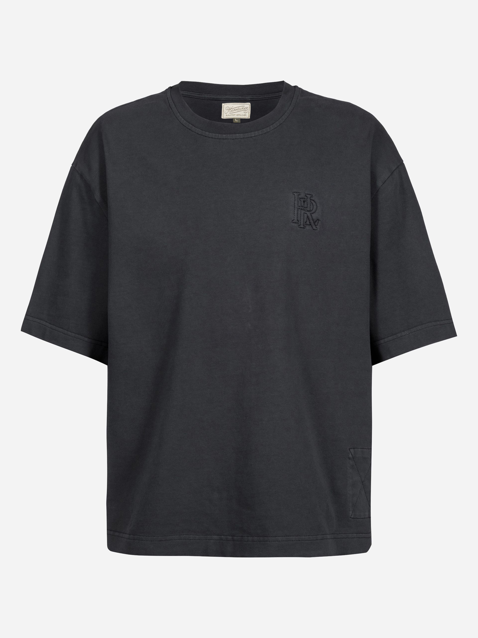 Schwarzes, locker sitzendes T-Shirt mit kurzen Ärmeln und einem kleinen gestickten Logo auf der linken Brust sowie einem Aufnäher auf der linken unteren Seite auf weißem Grund.