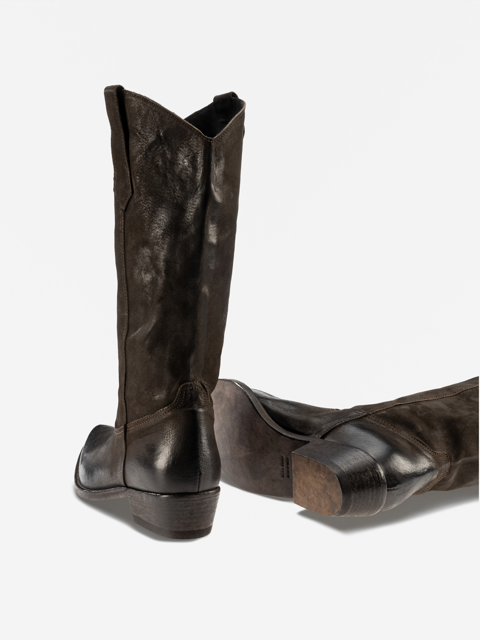 Ein Paar schwarze Cowboystiefel aus Leder, von denen einer aufrecht steht und der andere auf der Seite liegt, wobei die abgenutzte Sohle und der robuste Absatz zu sehen sind, vor einem schlichten weißen Hintergrund.