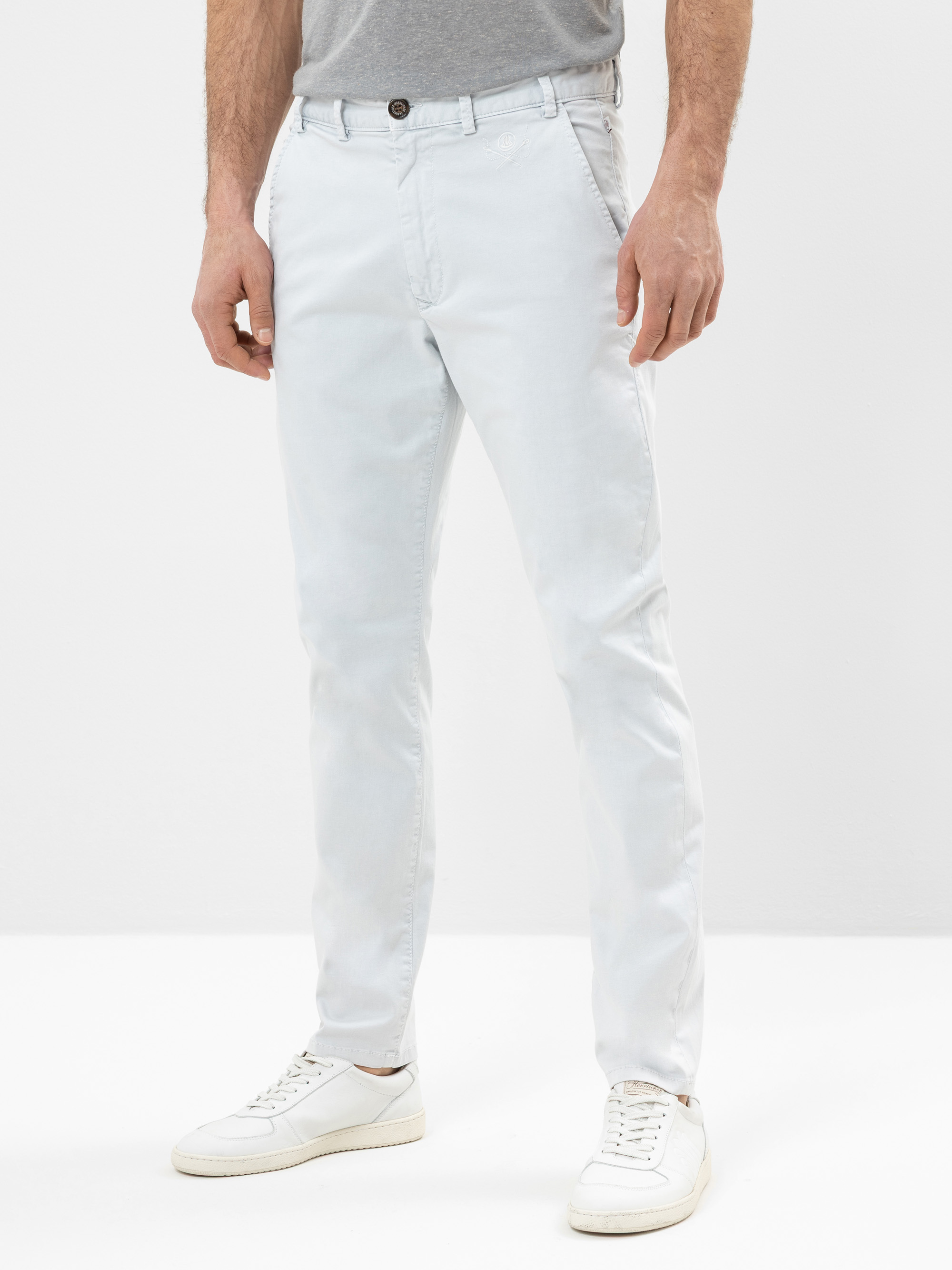 Ein Mann, der ein graues T-Shirt, eine helle, eng anliegende Hose und weiße Turnschuhe trägt, steht vor einem schlichten weißen Hintergrund. Sein Gesicht ist auf dem Bild nicht zu sehen.