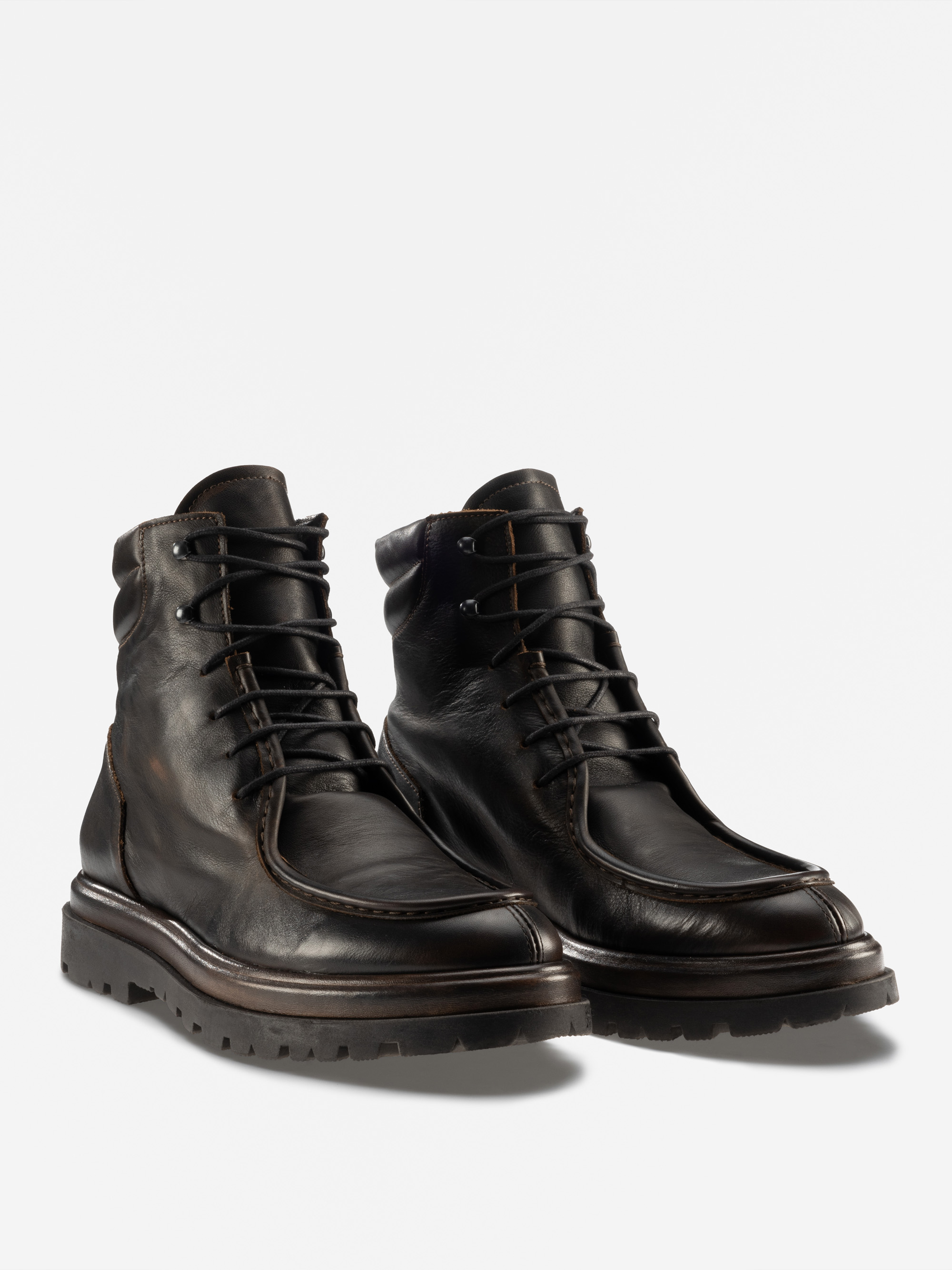 Ein Paar schwarze Lederschnürstiefel mit dicken, strukturierten Sohlen und sichtbaren Nähten, nebeneinander auf weißem Hintergrund.