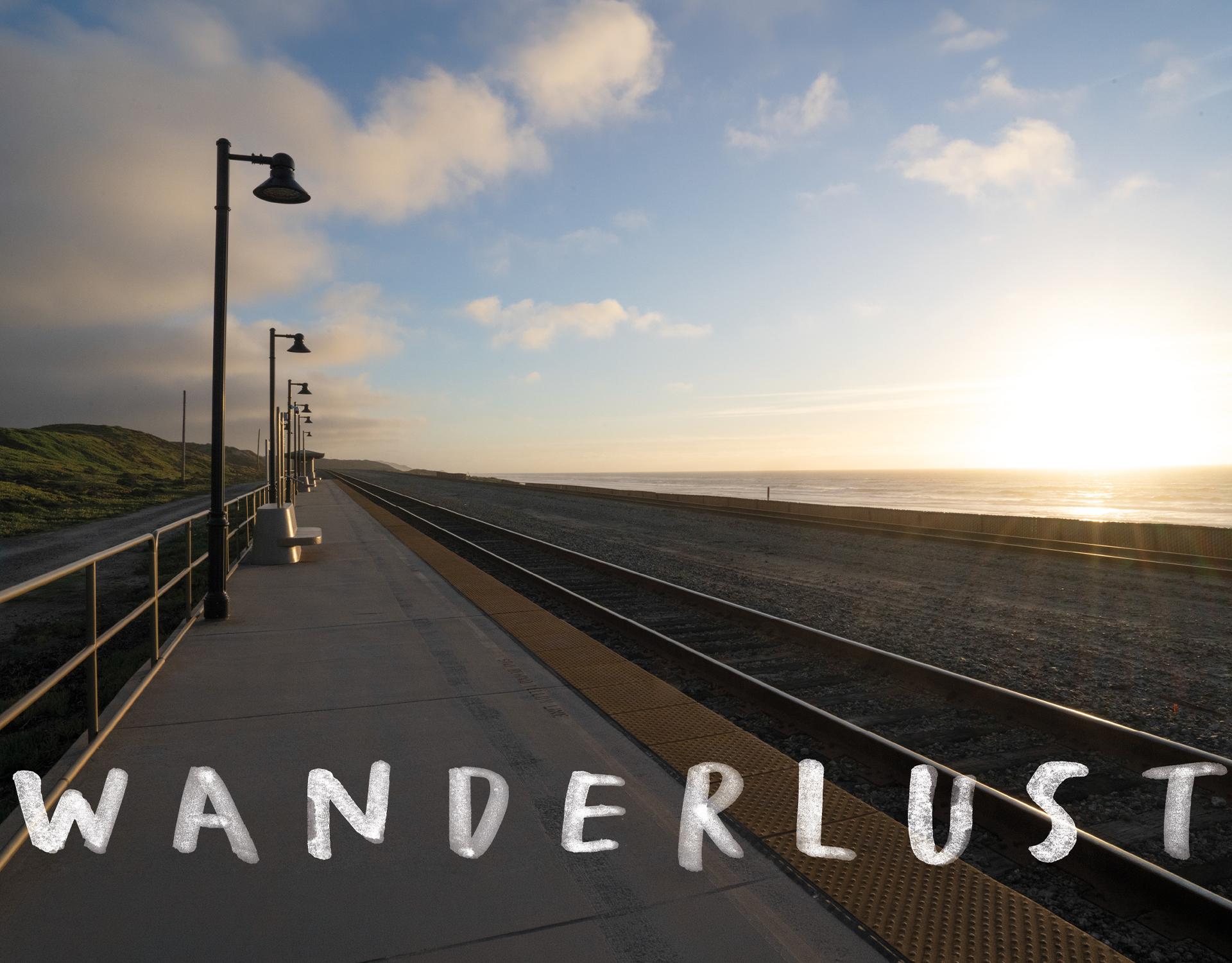 Ein sonnenbeschienener, leerer Bahnsteig neben den Gleisen erstreckt sich bis zum Horizont, am unteren Bildrand steht in fetten Buchstaben „WANDERLUST“. Der Himmel ist teilweise bewölkt, und links sind grasbewachsene Hügel zu sehen.