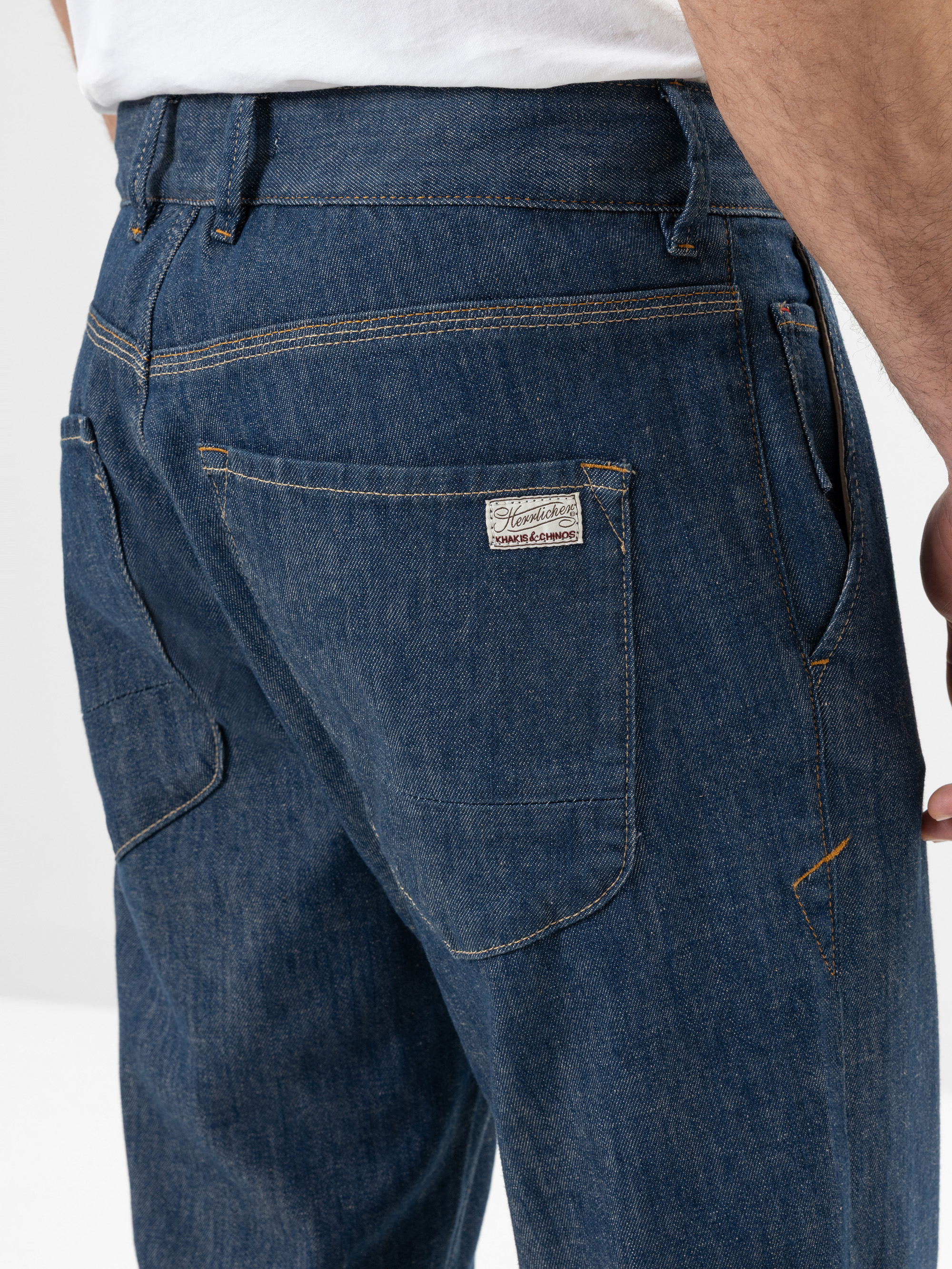 Nahaufnahme des Rückens einer Person, die Blue Denim Jeans und ein weißes Hemd trägt, mit Taschen, Nähten und einem kleinen Markenetikett auf der rechten Gesäßtasche.